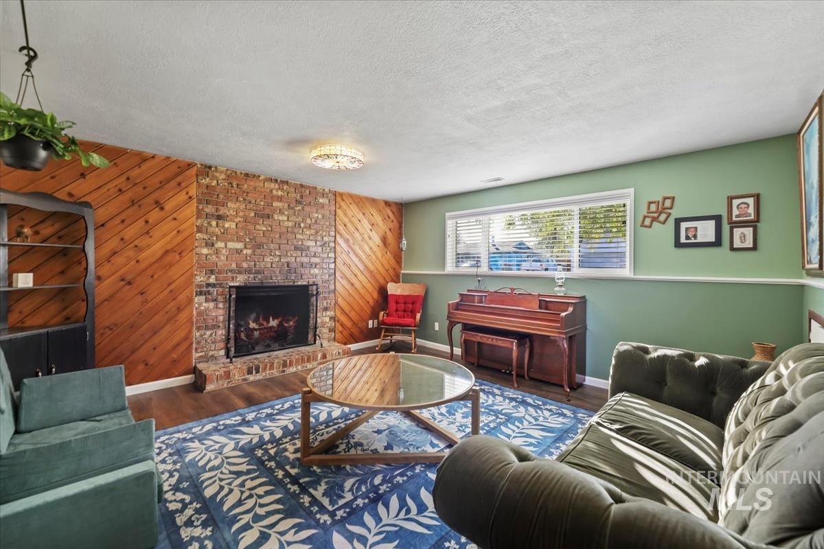 Living room with wood walls, a textured ceiling, wood finished floors, and a brick fireplace
