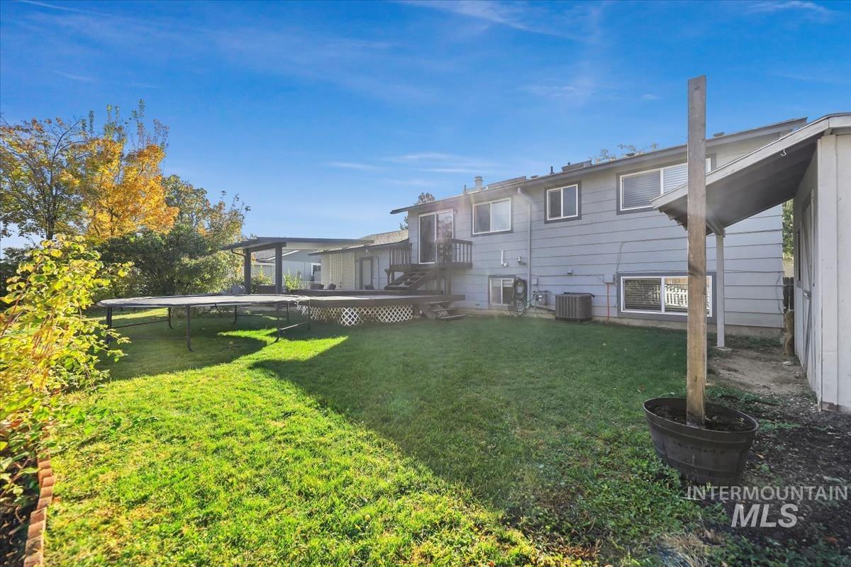 View of green lawn with a trampoline and a wooden deck