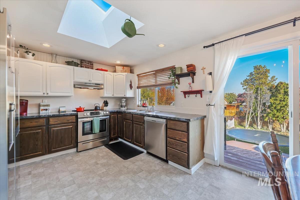 Kitchen featuring dark brown cabinetry, a skylight, appliances with stainless steel finishes, white cabinets, and under cabinet range hood
