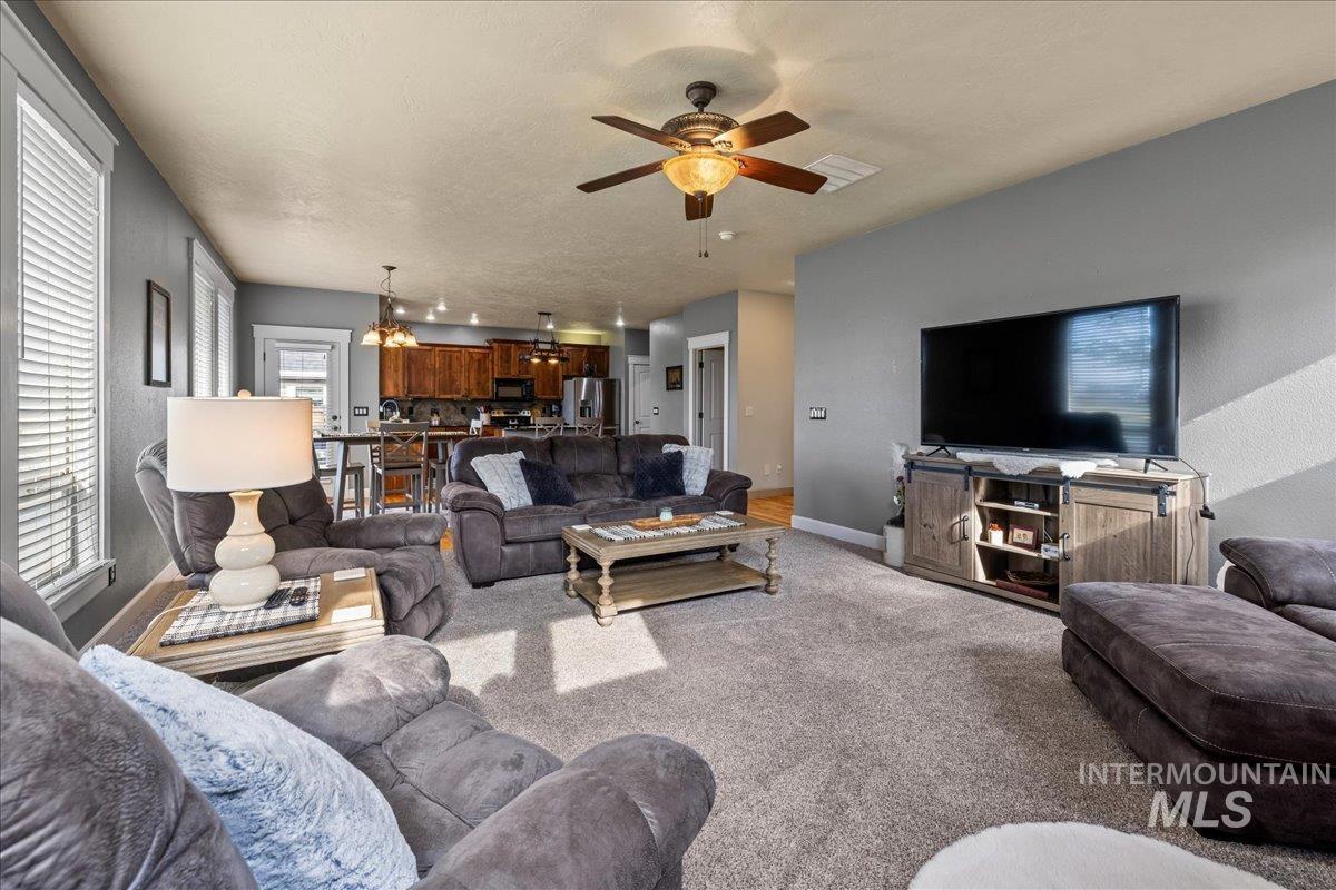 Living room featuring carpet, ceiling fan, a textured ceiling, and a chandelier