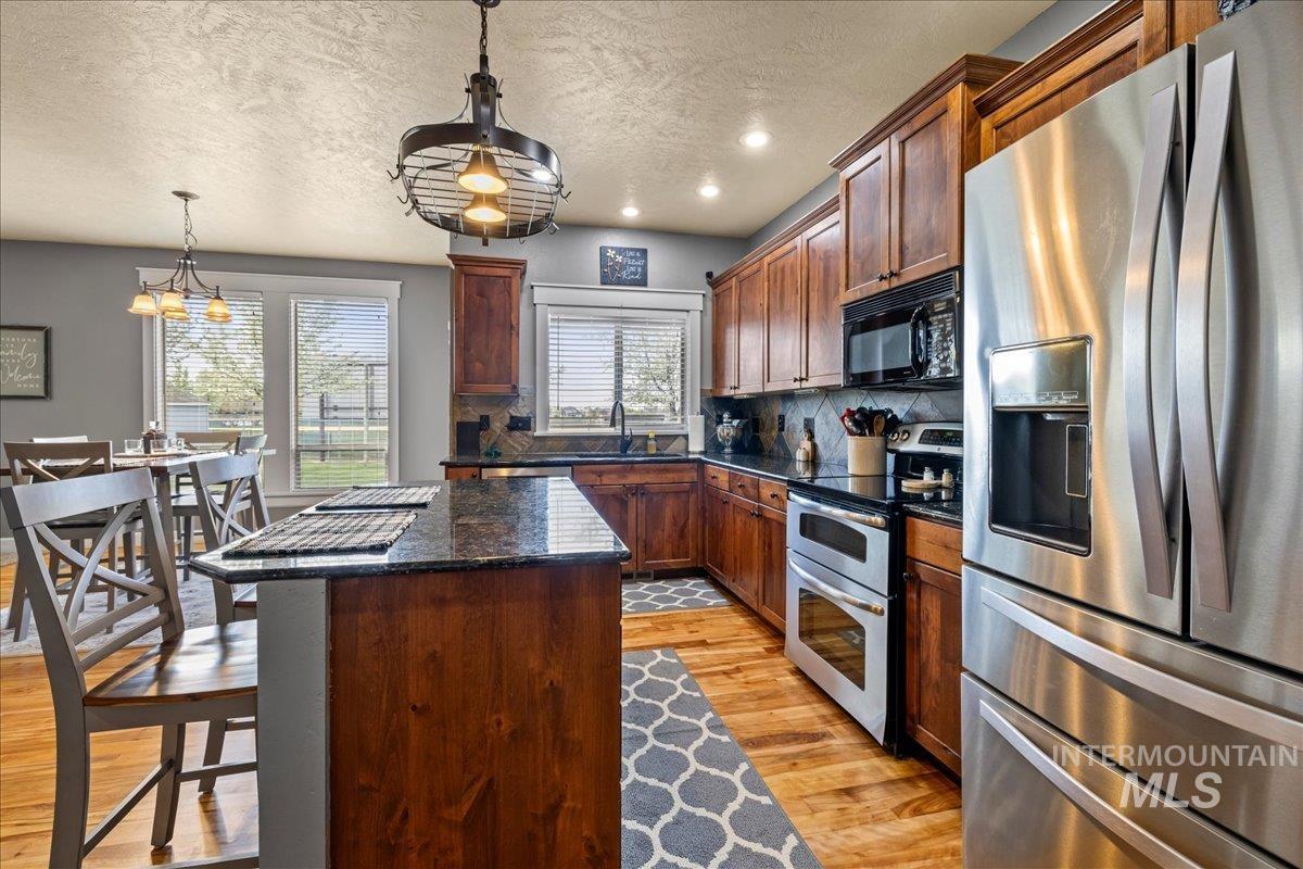 Kitchen featuring stainless steel appliances, dark stone counters, a textured ceiling, light wood-style flooring, and decorative backsplash