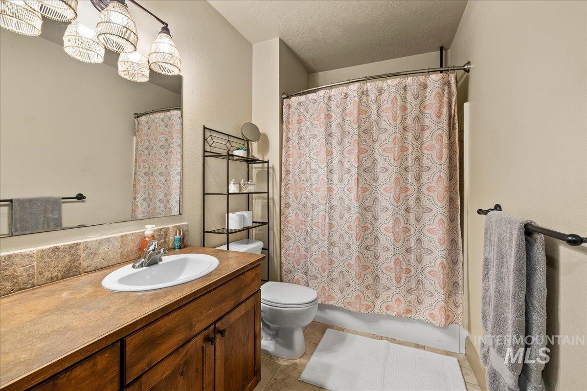 Bathroom with a textured ceiling, vanity, light tile patterned floors, and shower / bath combination with curtain