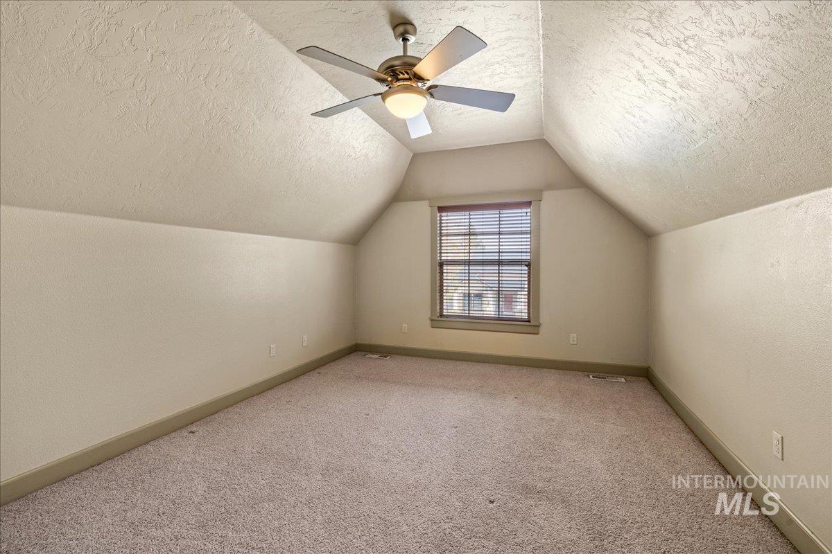 Bonus room featuring a textured ceiling, carpet floors, lofted ceiling, ceiling fan, and a textured wall