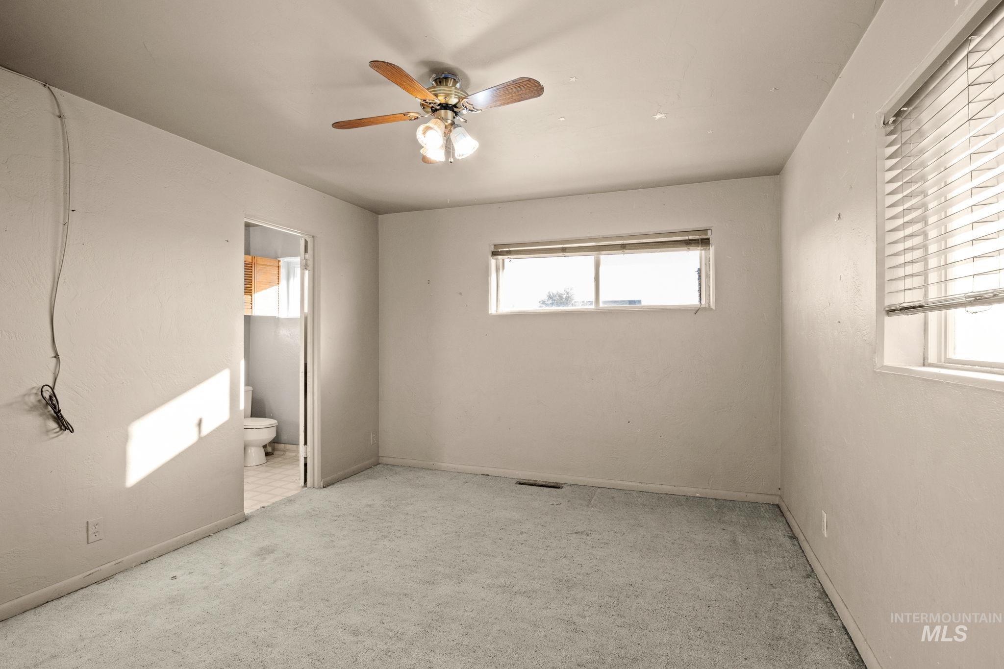 Unfurnished bedroom featuring carpet, multiple windows, ceiling fan, and ensuite bathroom