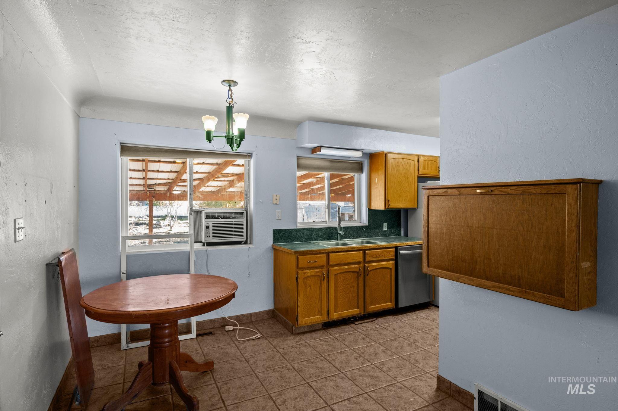 Kitchen featuring a textured wall, brown cabinets, a chandelier, hanging light fixtures, and dishwasher