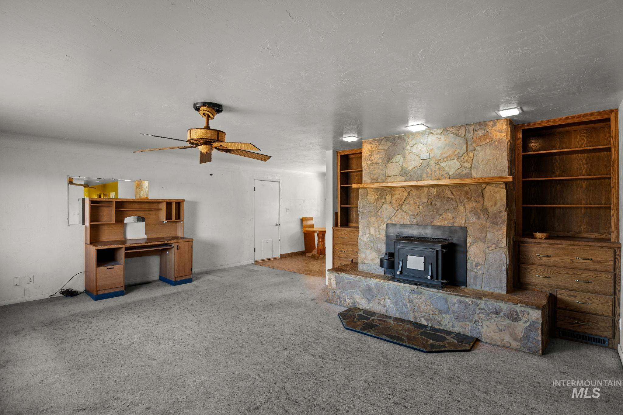 Unfurnished living room featuring a wood stove, carpet floors, built in features, and a ceiling fan