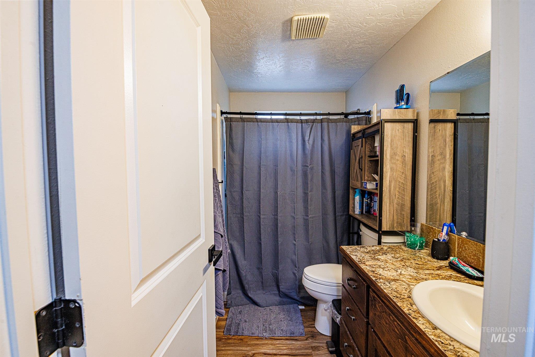 Bathroom featuring a textured ceiling, dark wood-style floors, a shower with curtain, and vanity