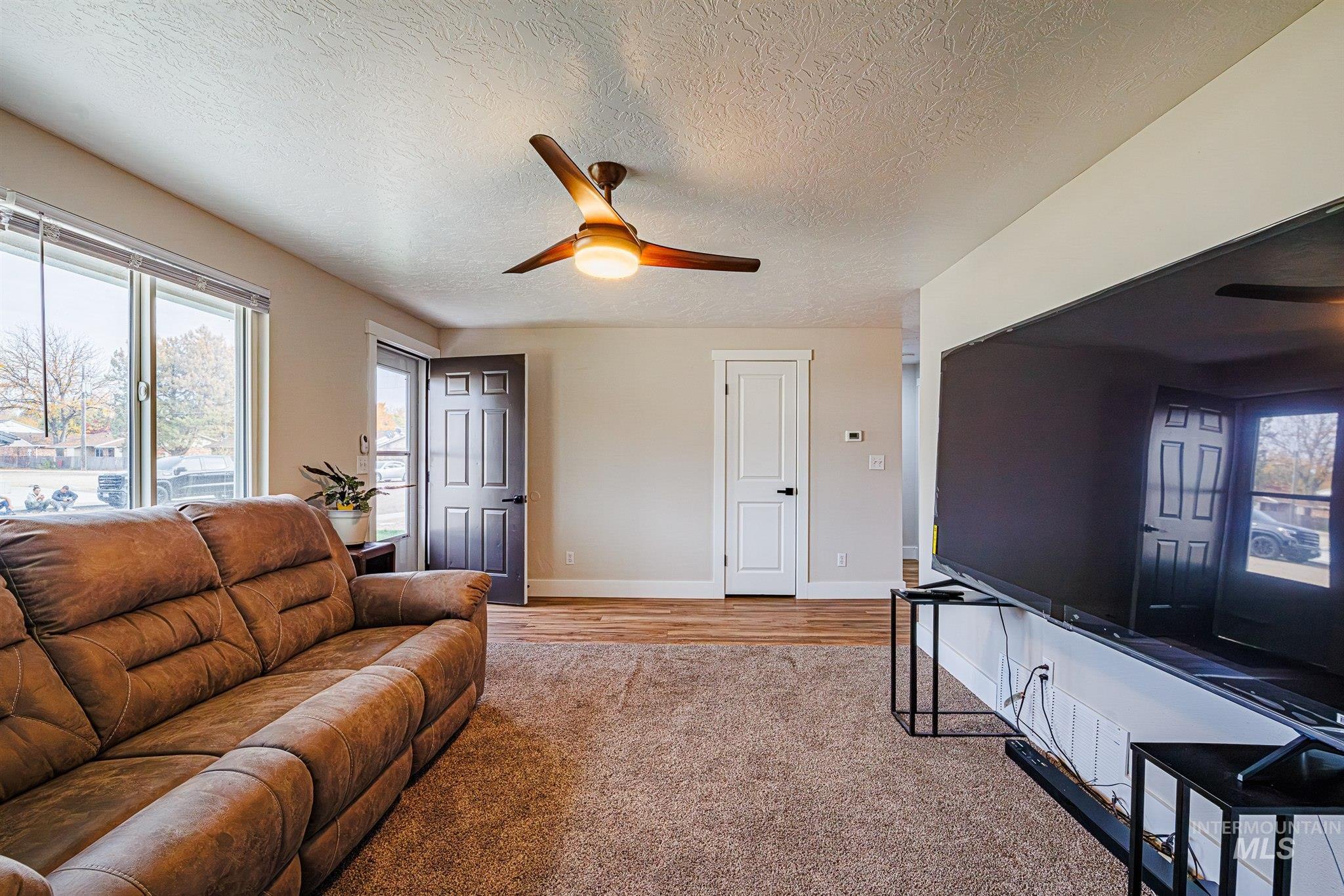 Living area with a ceiling fan, a textured ceiling, and light wood-style floors
