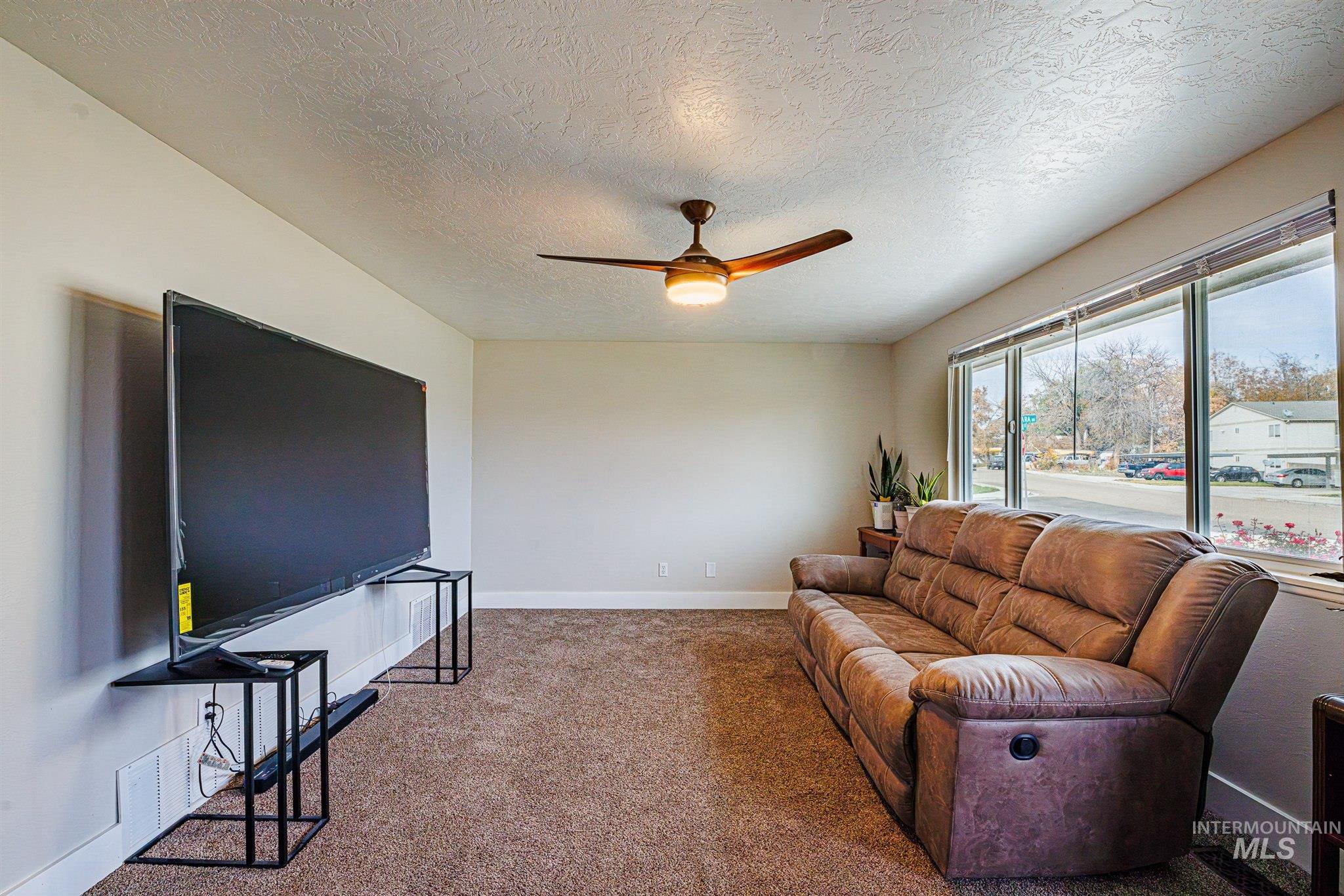 Living area featuring a ceiling fan, carpet flooring, and a textured ceiling