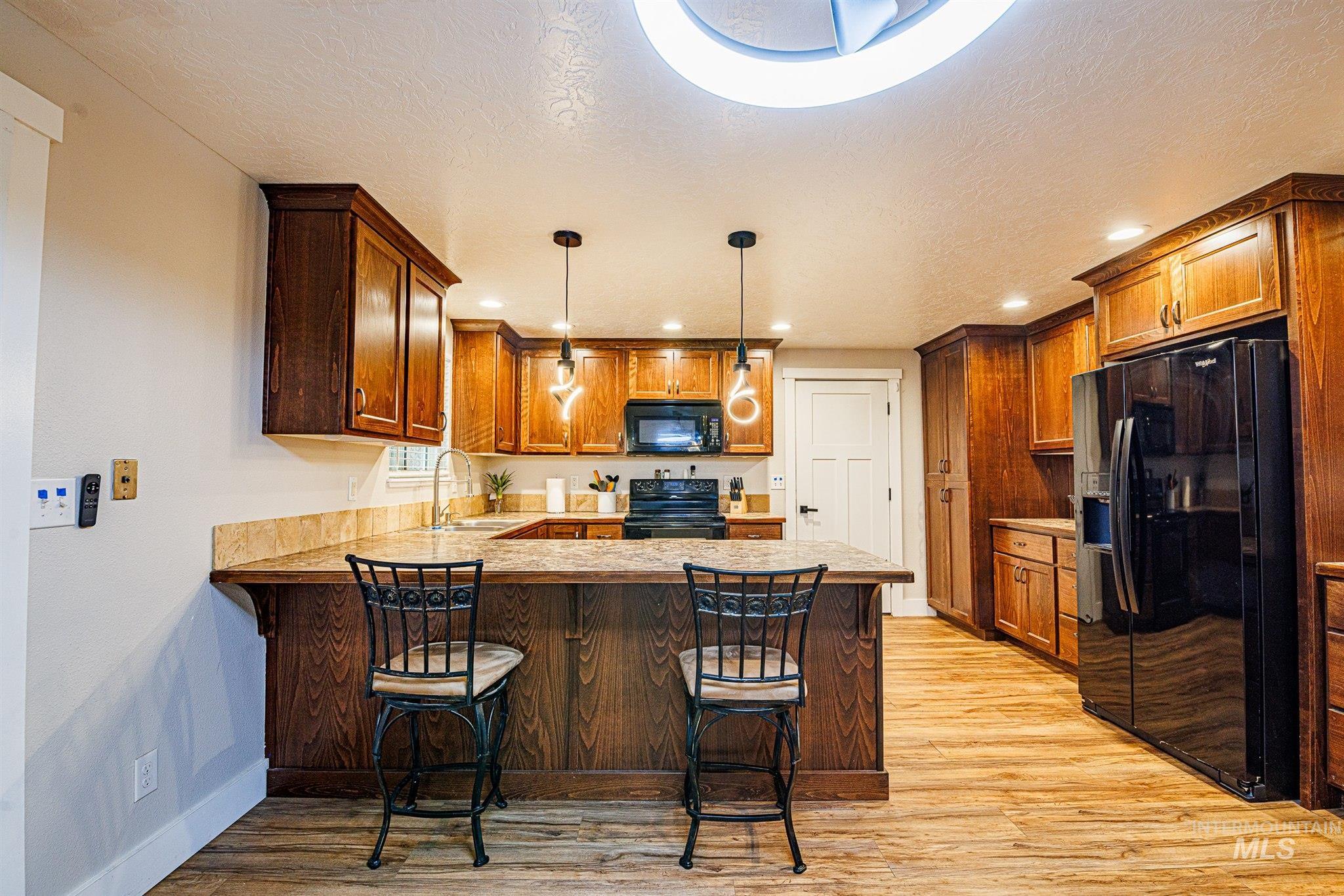 Kitchen with a breakfast bar, black appliances, a peninsula, light wood-style flooring, and a textured ceiling