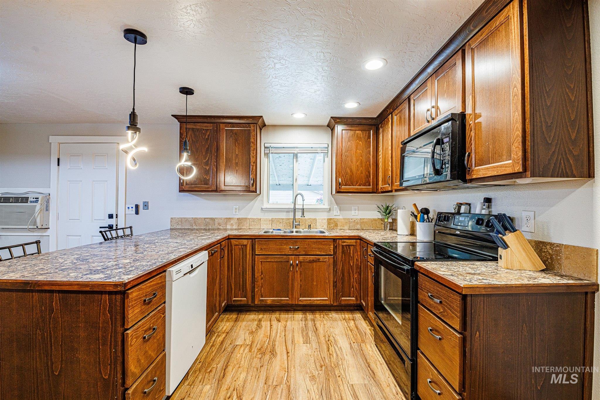 Kitchen featuring black appliances, brown cabinetry, light wood-type flooring, hanging light fixtures, and a textured ceiling