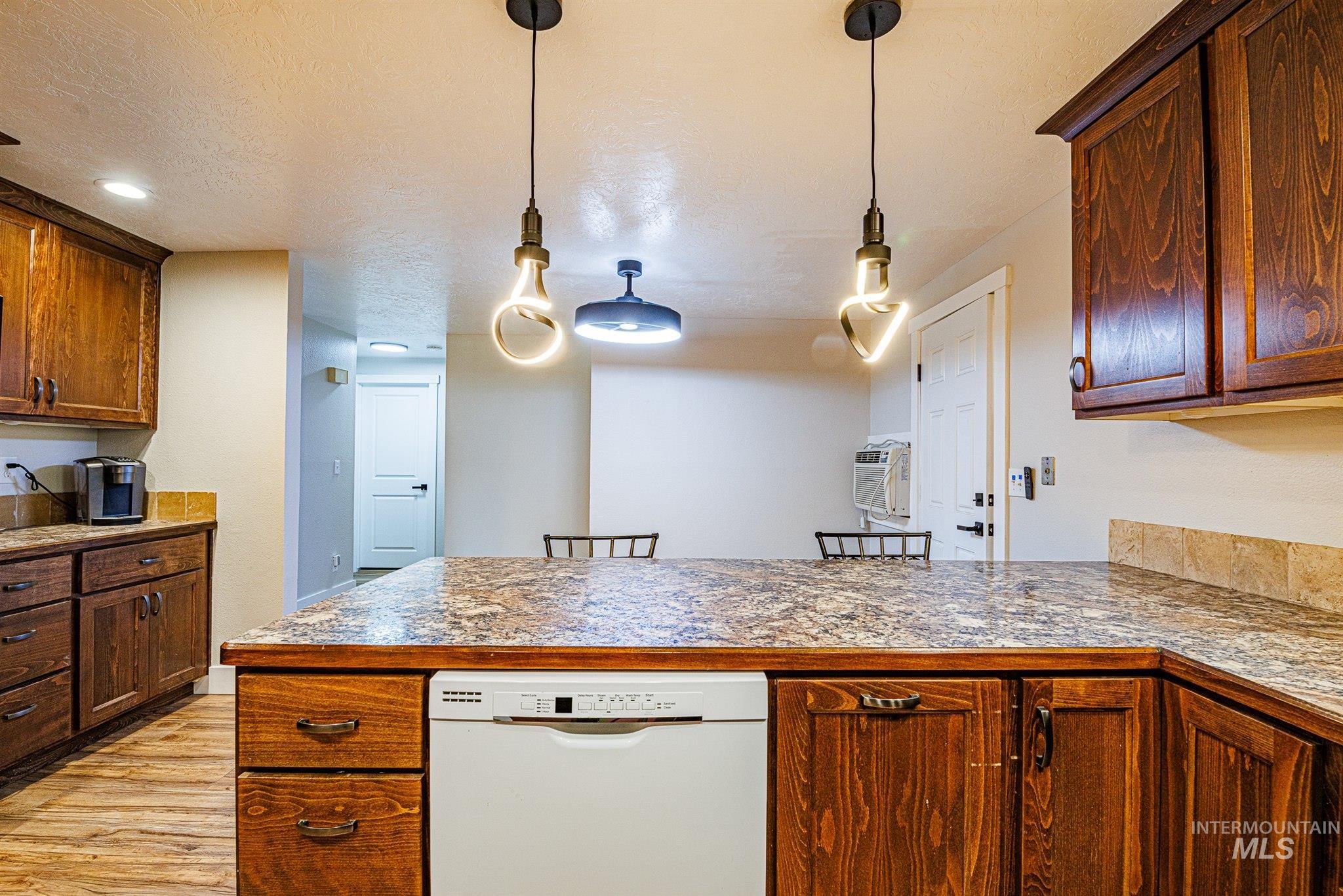 Kitchen with white dishwasher, a textured ceiling, decorative light fixtures, light wood-type flooring, and a peninsula