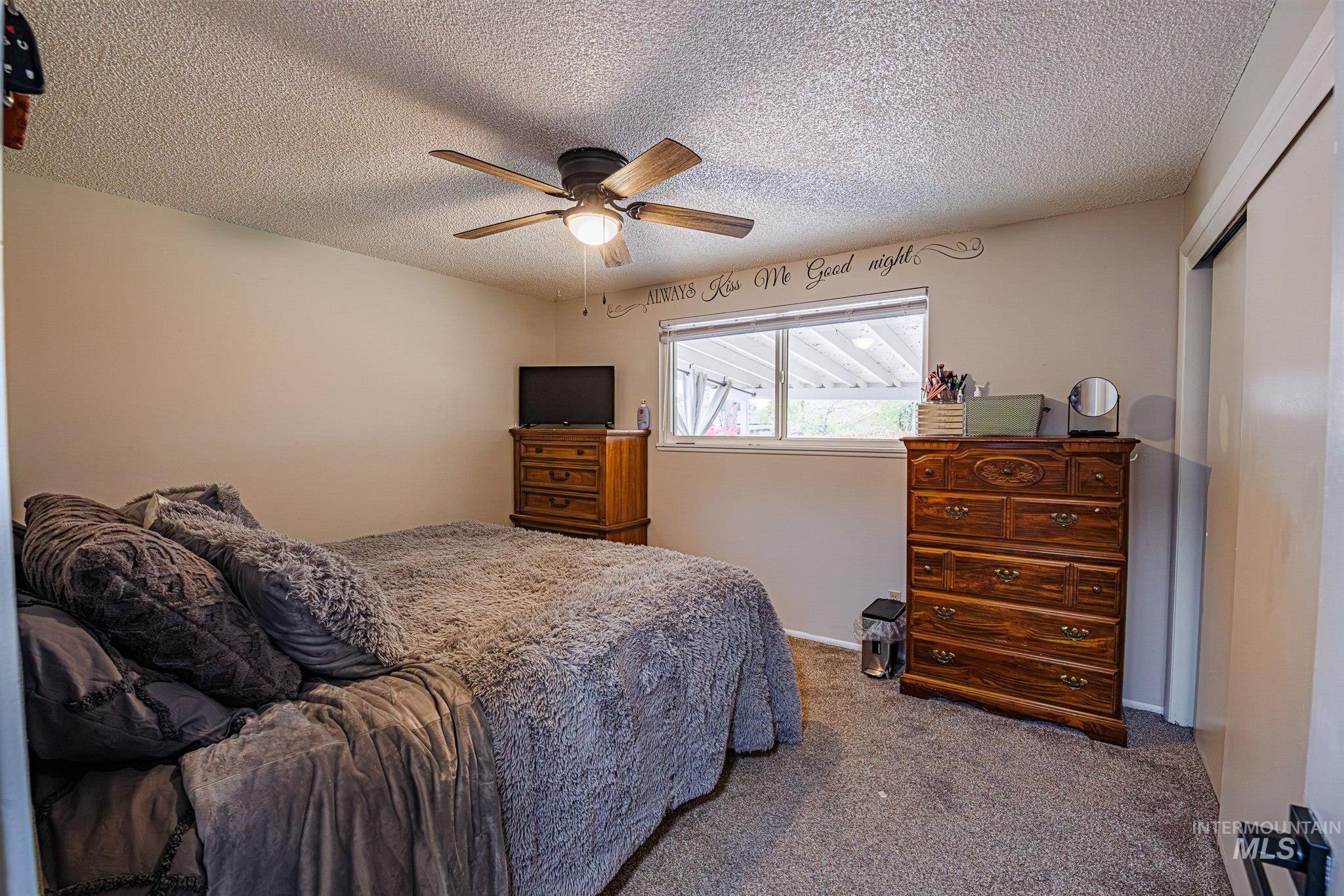 Carpeted bedroom with a textured ceiling, ceiling fan, and a closet