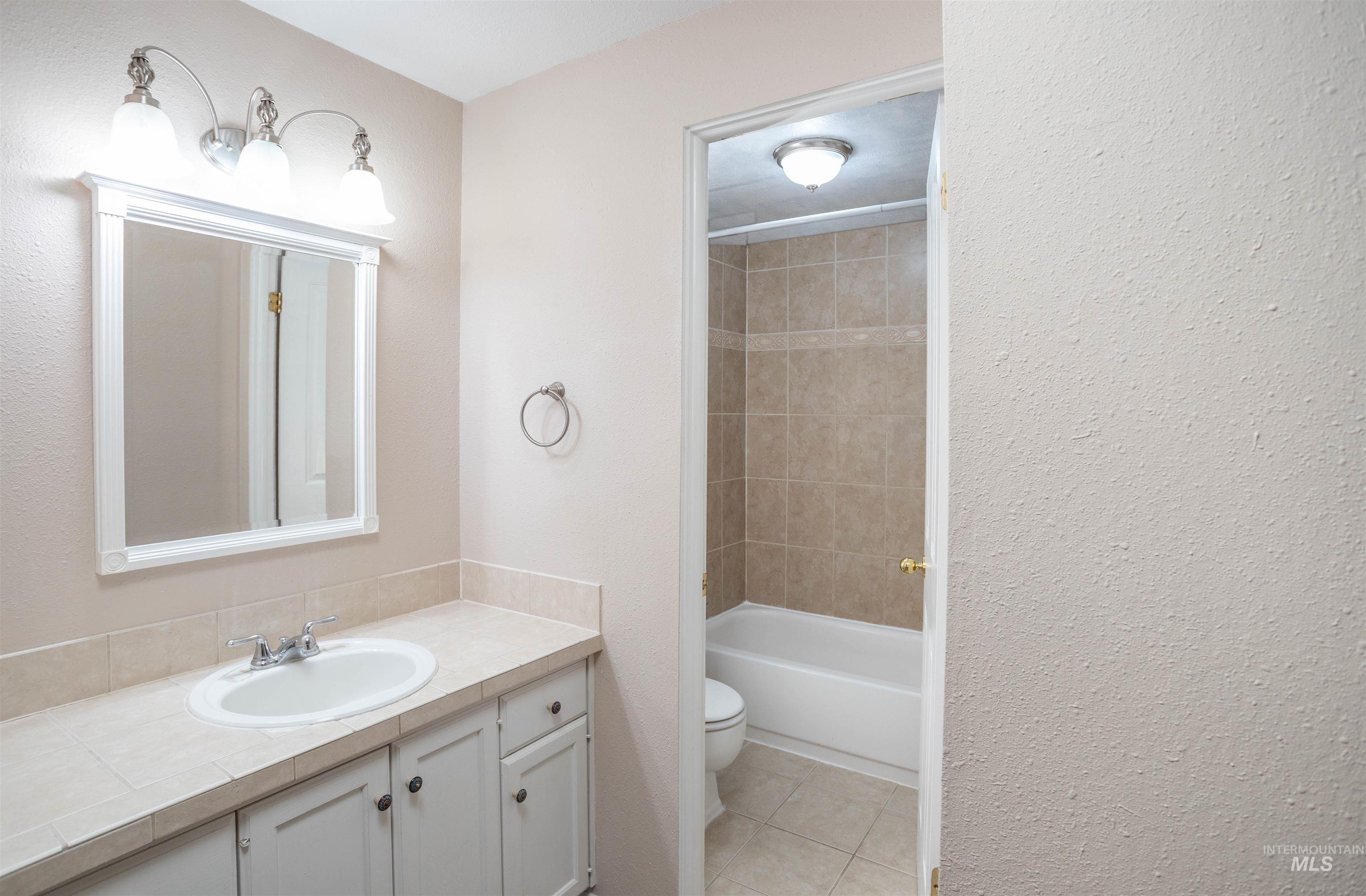 Bathroom featuring vanity, light tile patterned floors, a textured wall, and tub / shower combination