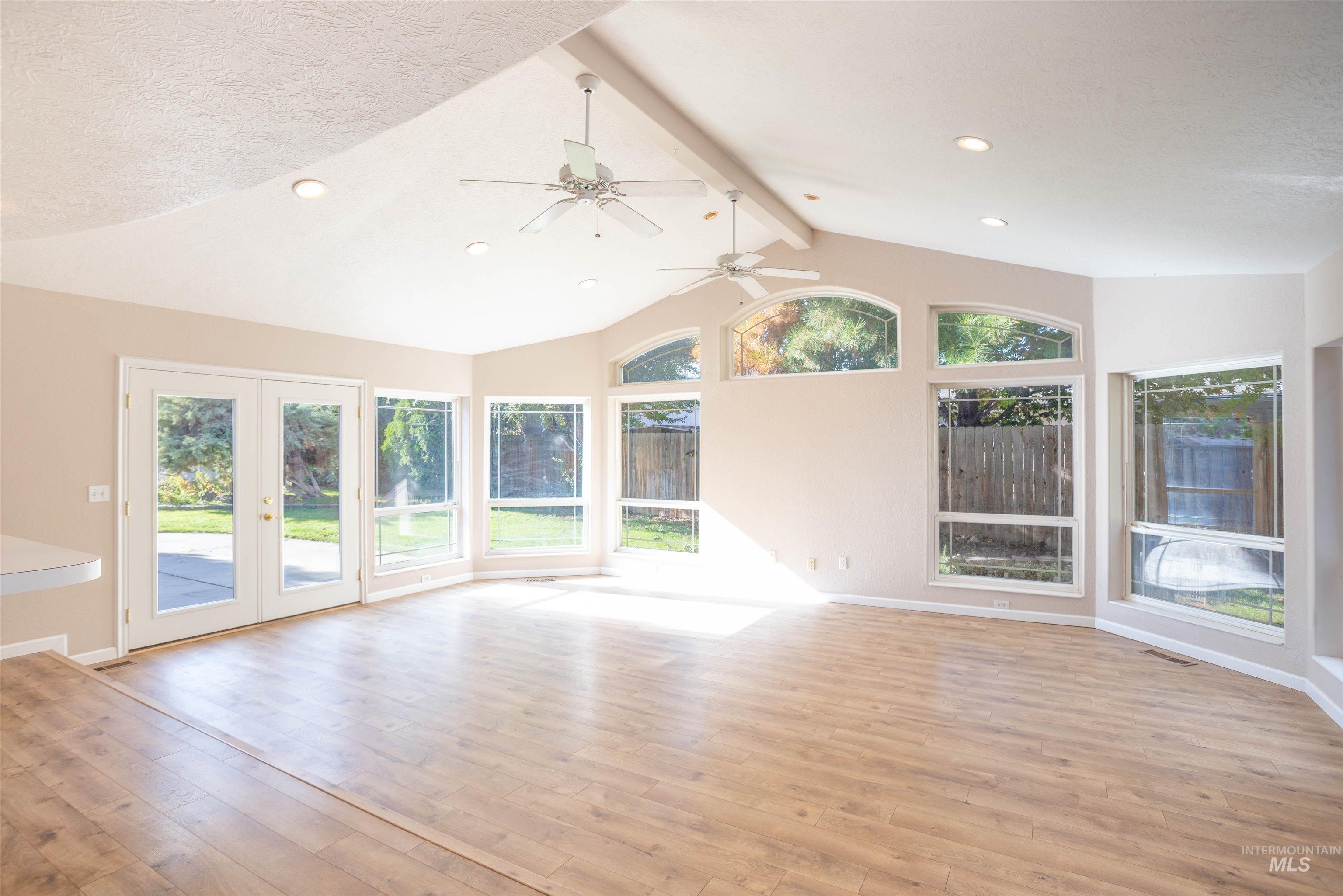 Unfurnished living room featuring beamed ceiling, plenty of natural light, french doors, light wood-style flooring, and recessed lighting