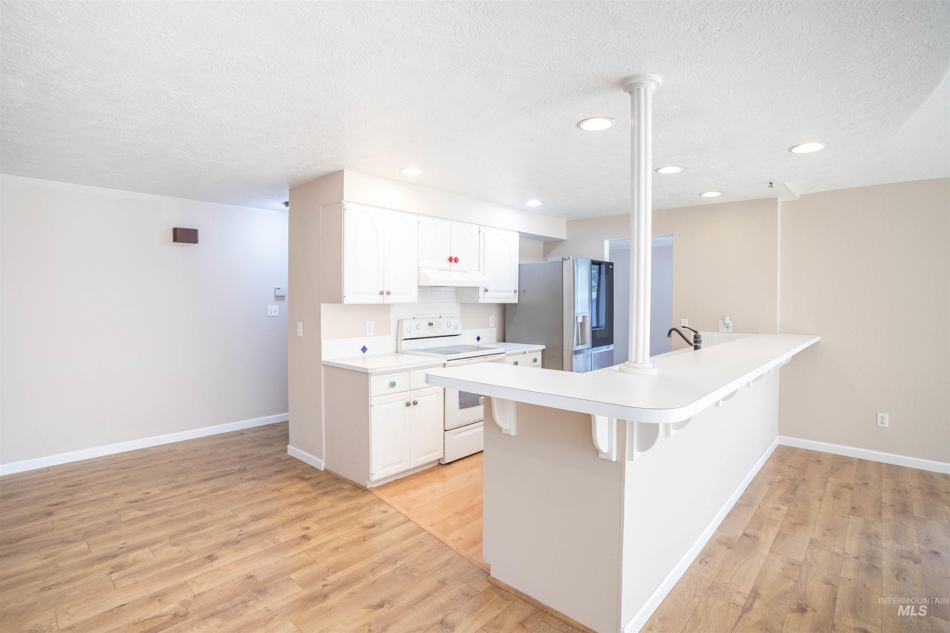 Kitchen with light countertops, white range with electric stovetop, a breakfast bar area, white cabinetry, and stainless steel fridge with ice dispenser