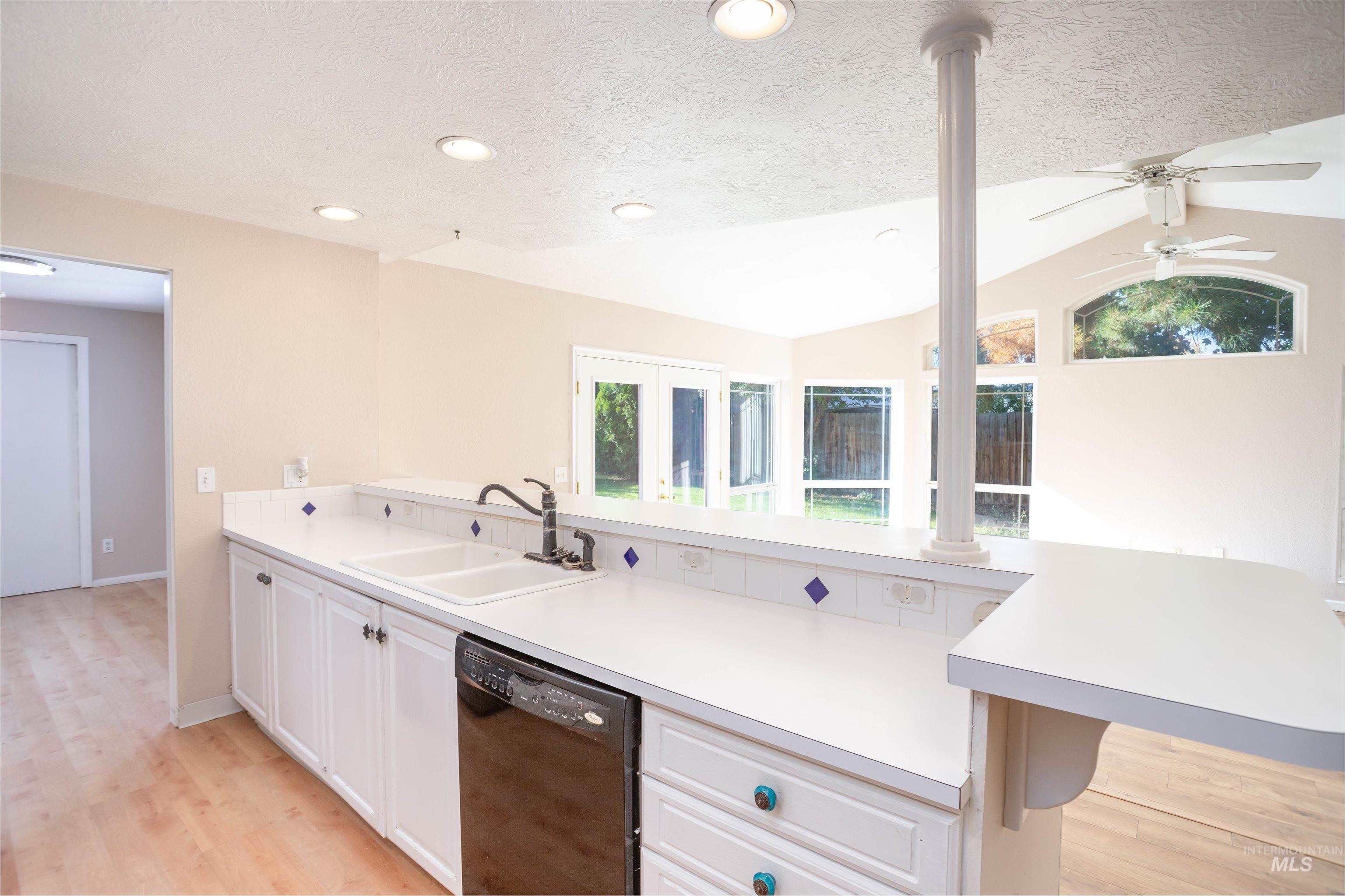 Kitchen with light countertops, a peninsula, white cabinets, dishwasher, and lofted ceiling