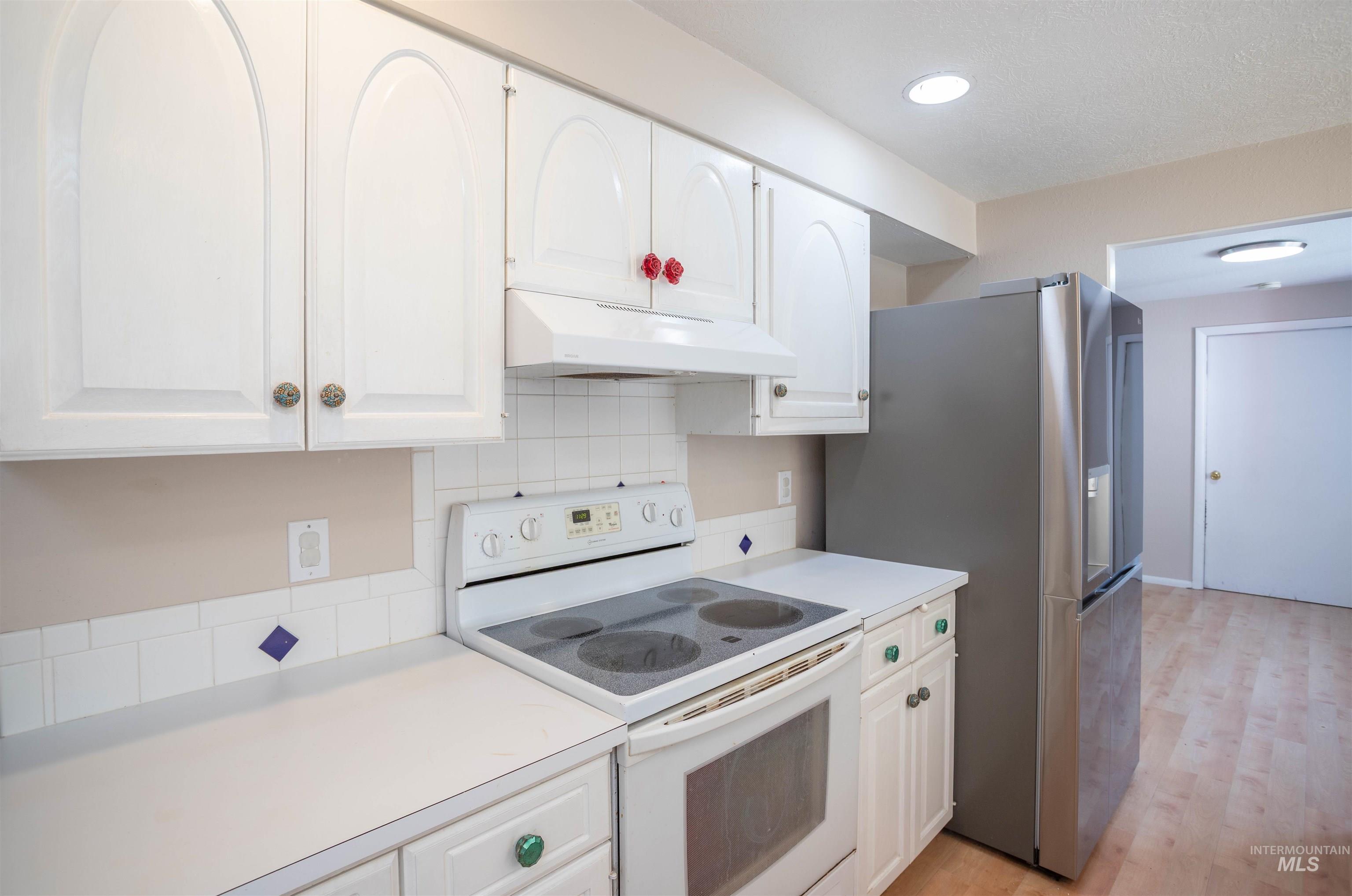 Kitchen featuring white range with electric stovetop, white cabinetry, light countertops, backsplash, and light wood-style flooring