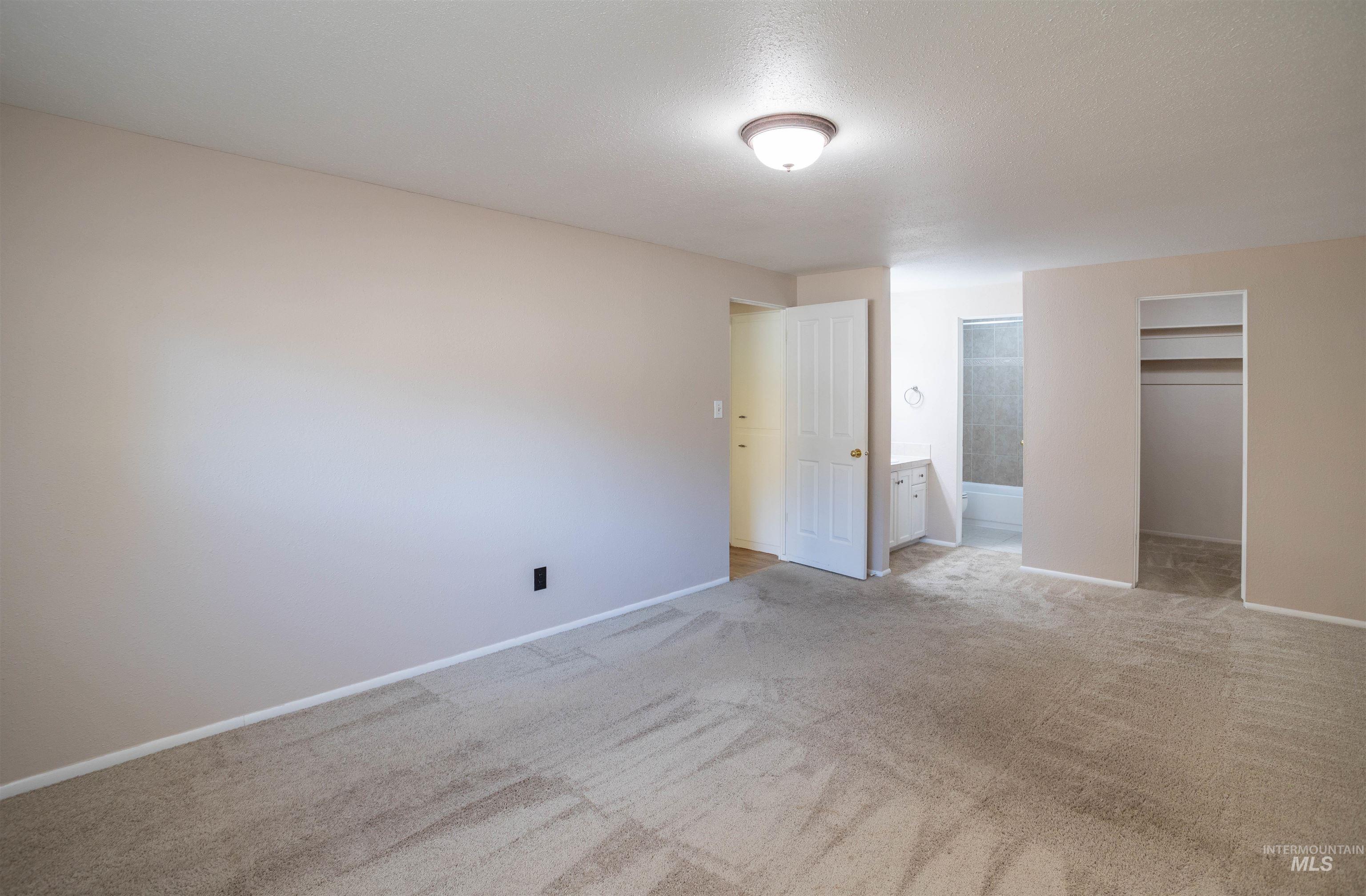 Unfurnished bedroom with a spacious closet, light colored carpet, and connected bathroom