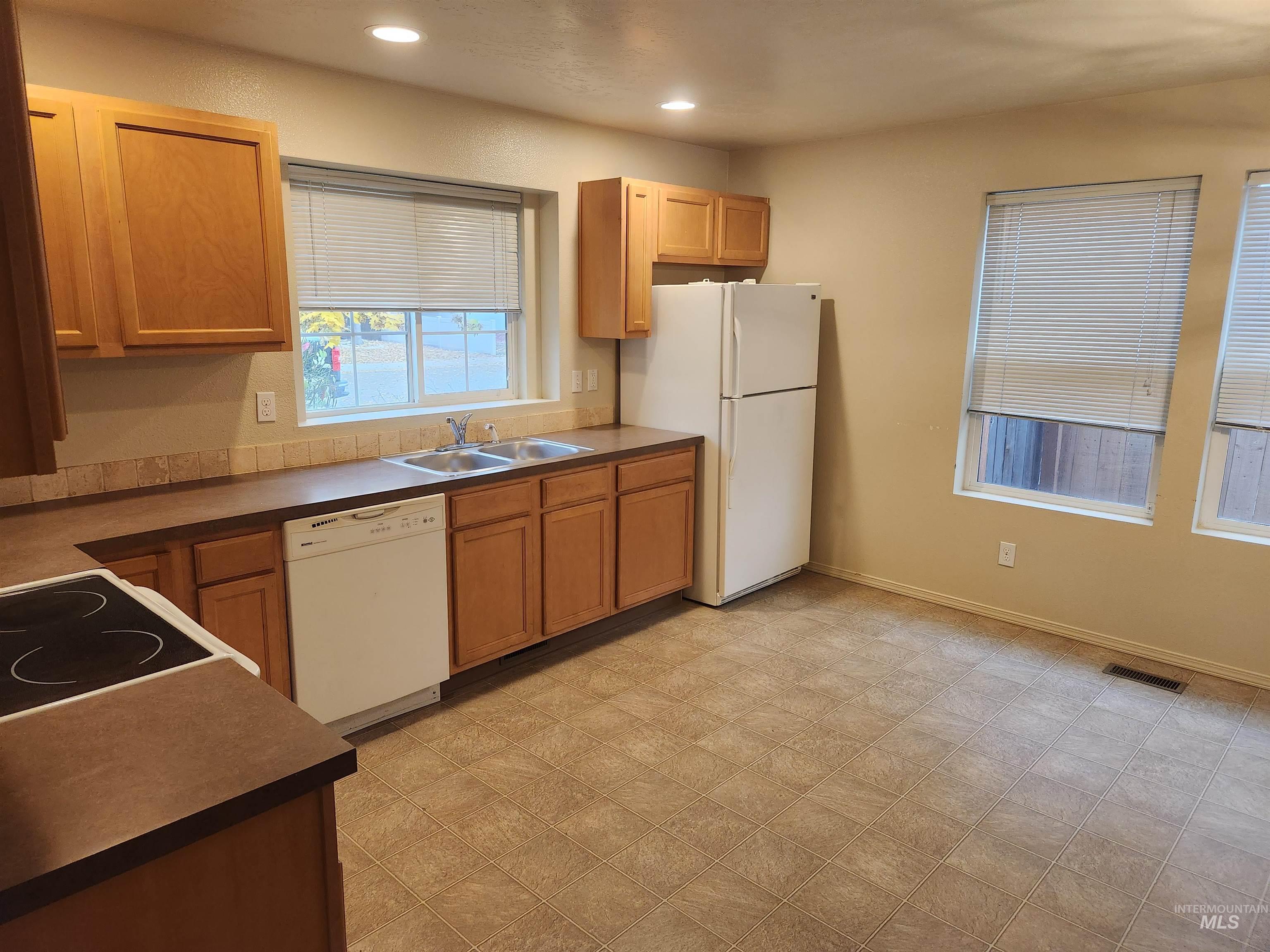 Kitchen featuring dark countertops, white appliances, recessed lighting, light flooring, and brown cabinets
