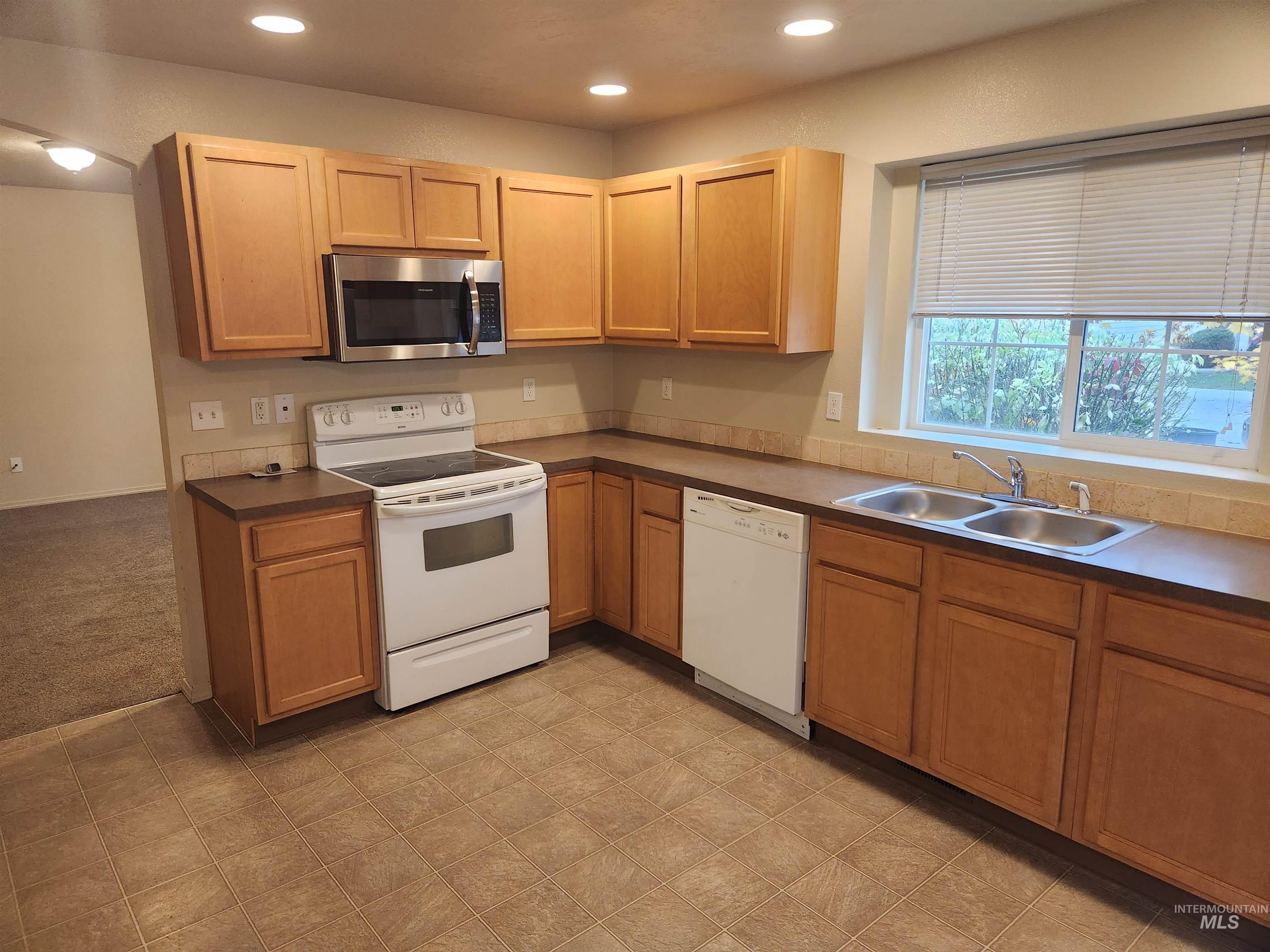 Kitchen with white appliances, recessed lighting, dark countertops, and light carpet