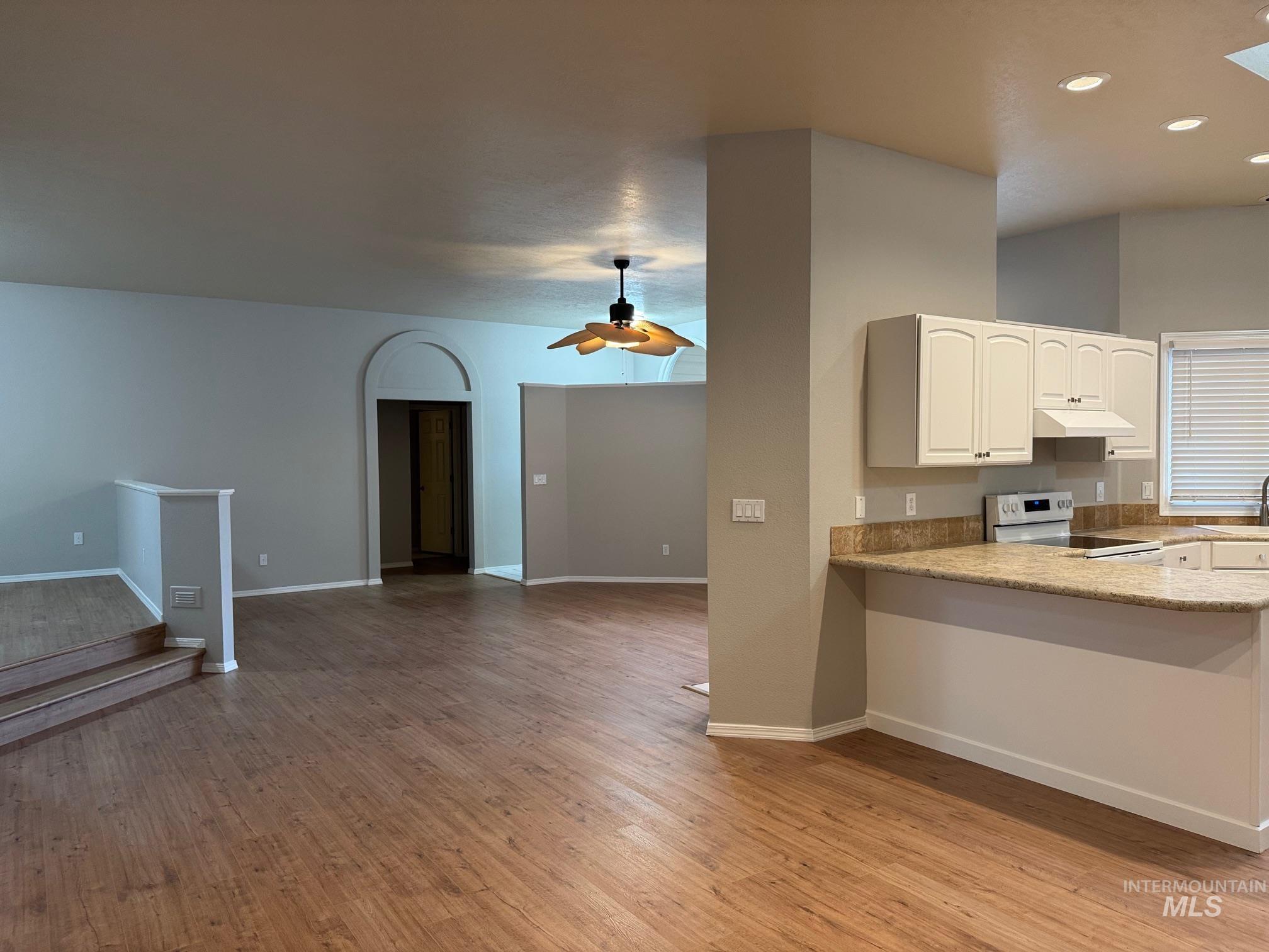 Kitchen with white electric stove, light wood-type flooring, open floor plan, white cabinets, and light stone counters