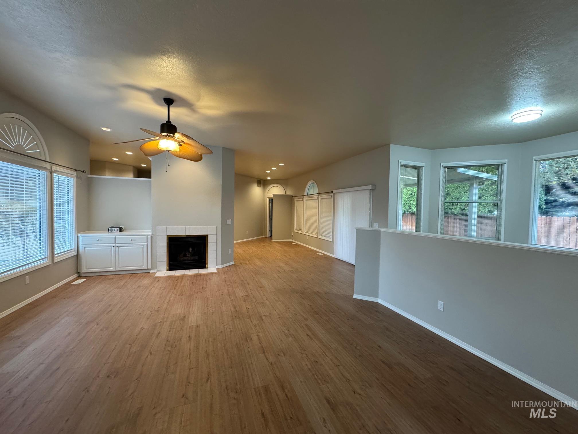 Unfurnished living room with wood finished floors, a tiled fireplace, ceiling fan, a textured ceiling, and recessed lighting