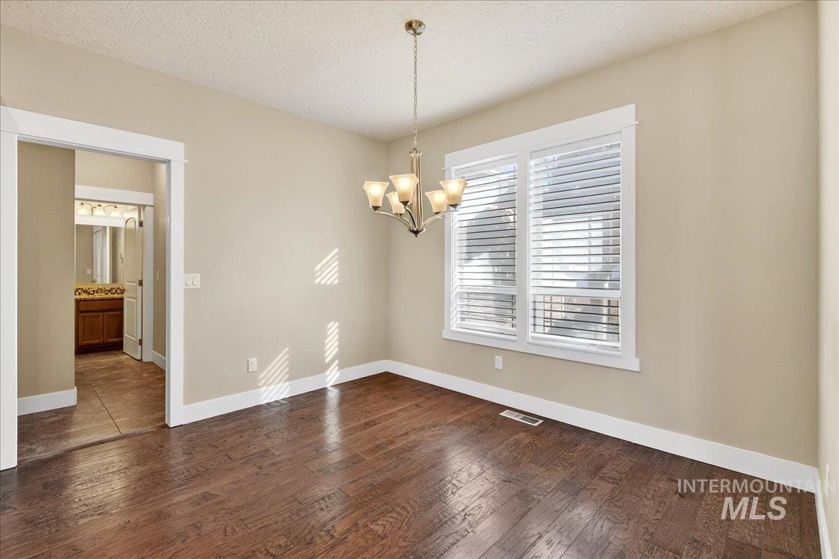Unfurnished dining area featuring a textured ceiling, dark wood-style floors, and a chandelier