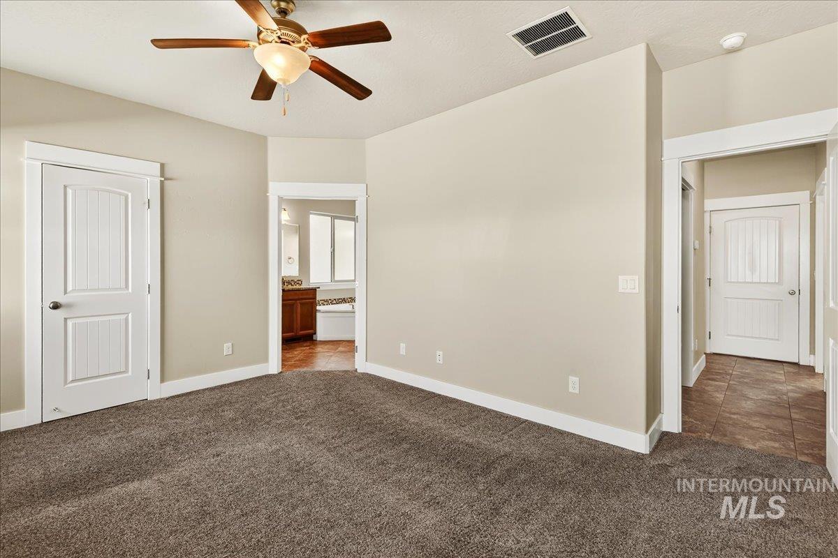 Unfurnished bedroom featuring ensuite bathroom, carpet flooring, tile patterned flooring, and ceiling fan