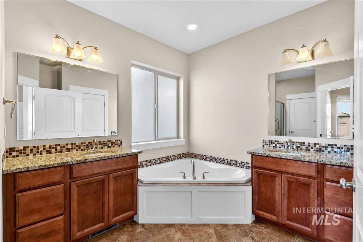Bathroom with decorative backsplash, a garden tub, two vanities, and recessed lighting