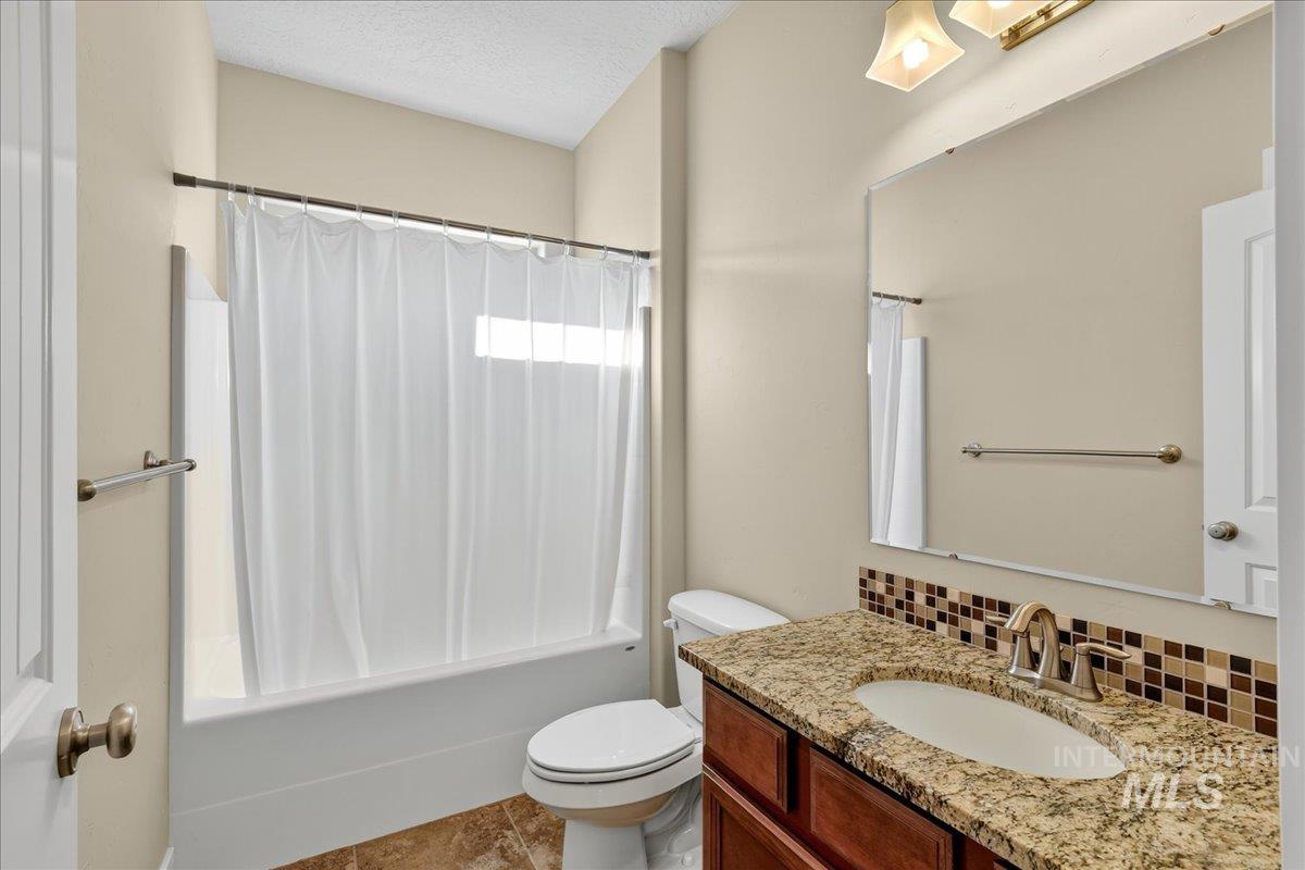 Bathroom with shower / bath combo with shower curtain, a textured ceiling, vanity, tasteful backsplash, and light tile patterned flooring