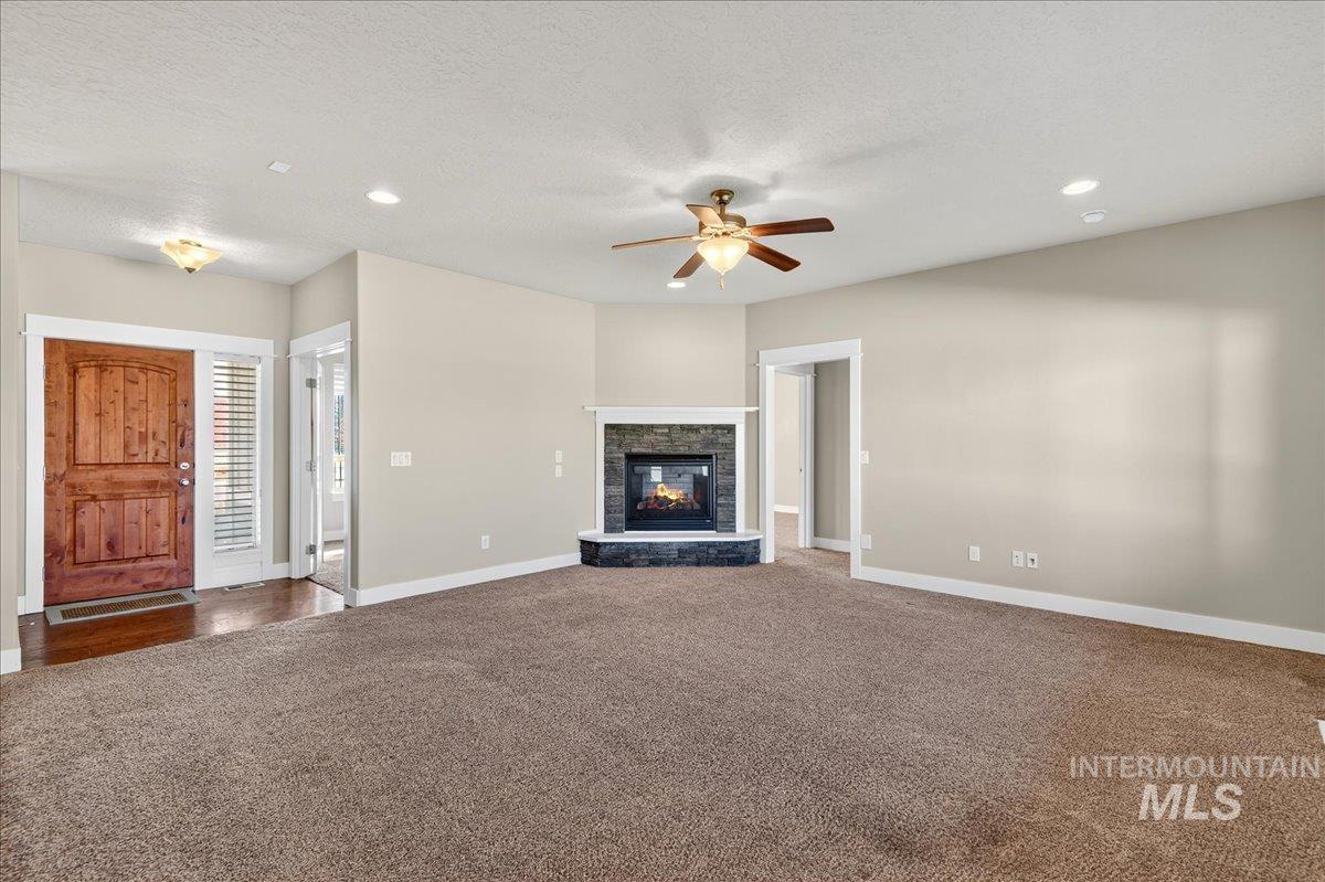 Unfurnished living room with dark carpet, a fireplace, a textured ceiling, ceiling fan, and recessed lighting