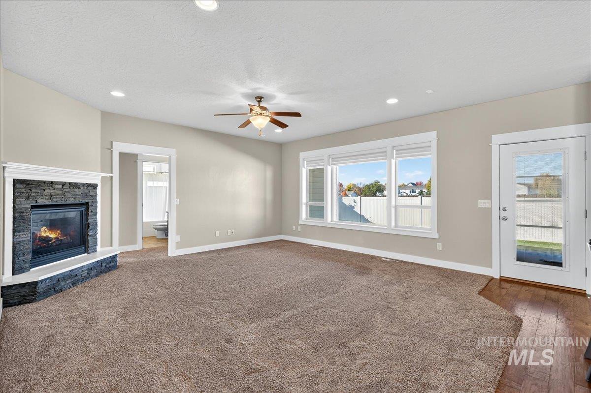 Unfurnished living room with ceiling fan, recessed lighting, a stone fireplace, dark colored carpet, and a textured ceiling
