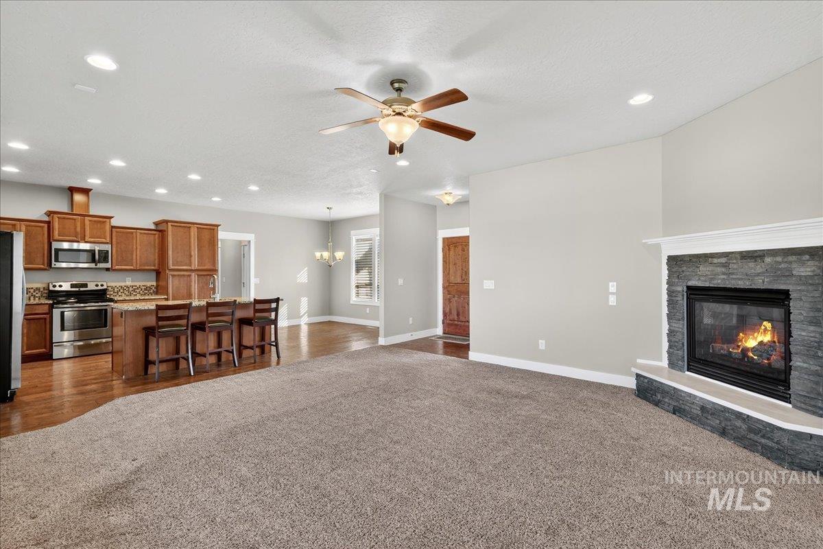 Living area featuring a chandelier, dark colored carpet, recessed lighting, ceiling fan, and a fireplace