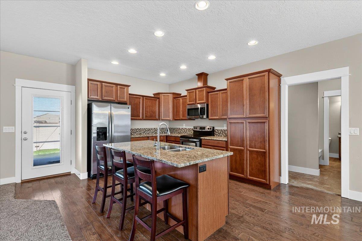 Kitchen featuring appliances with stainless steel finishes, recessed lighting, a breakfast bar area, dark wood finished floors, and a textured ceiling