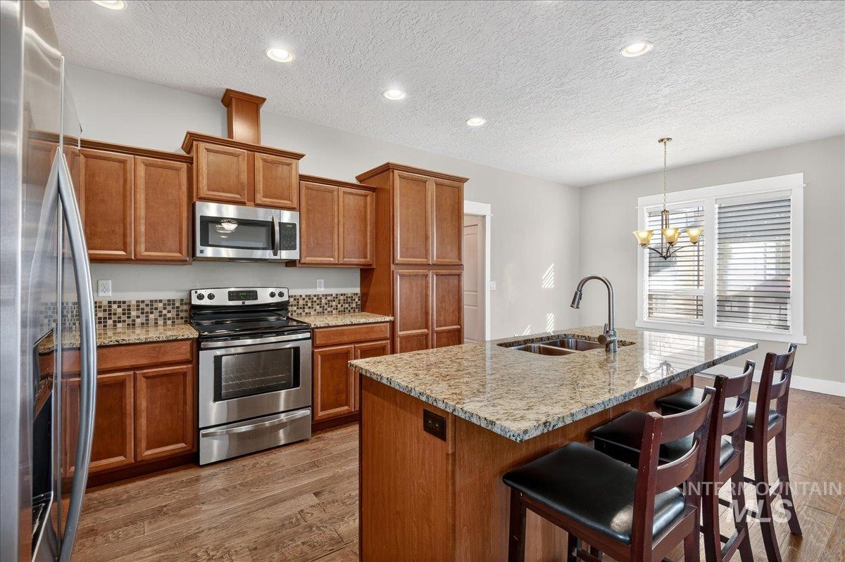 Kitchen with brown cabinetry, stainless steel appliances, dark wood finished floors, light stone countertops, and a textured ceiling
