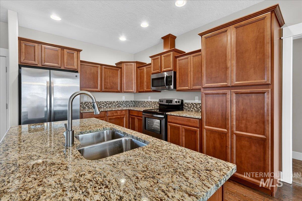 Kitchen featuring stainless steel appliances, brown cabinets, light stone countertops, a textured ceiling, and recessed lighting