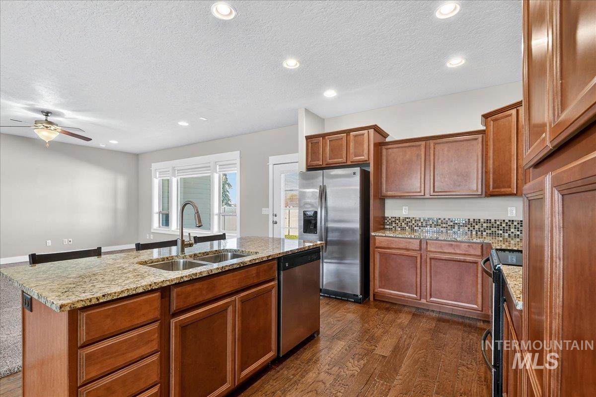 Kitchen with recessed lighting, stainless steel appliances, brown cabinets, light stone countertops, and dark wood-style floors