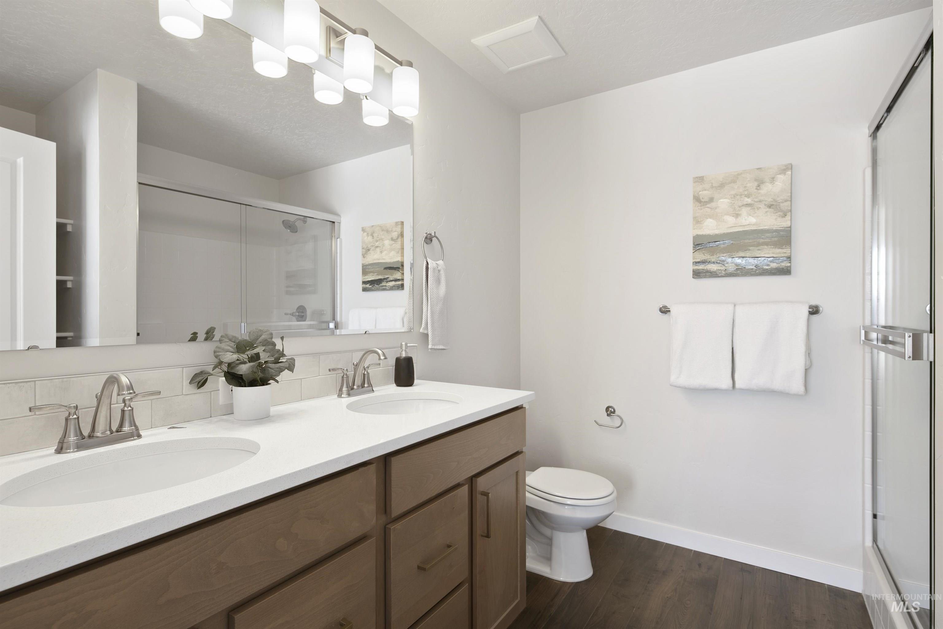 Full bath featuring dark wood-style floors, a shower stall, double vanity, and tasteful backsplash