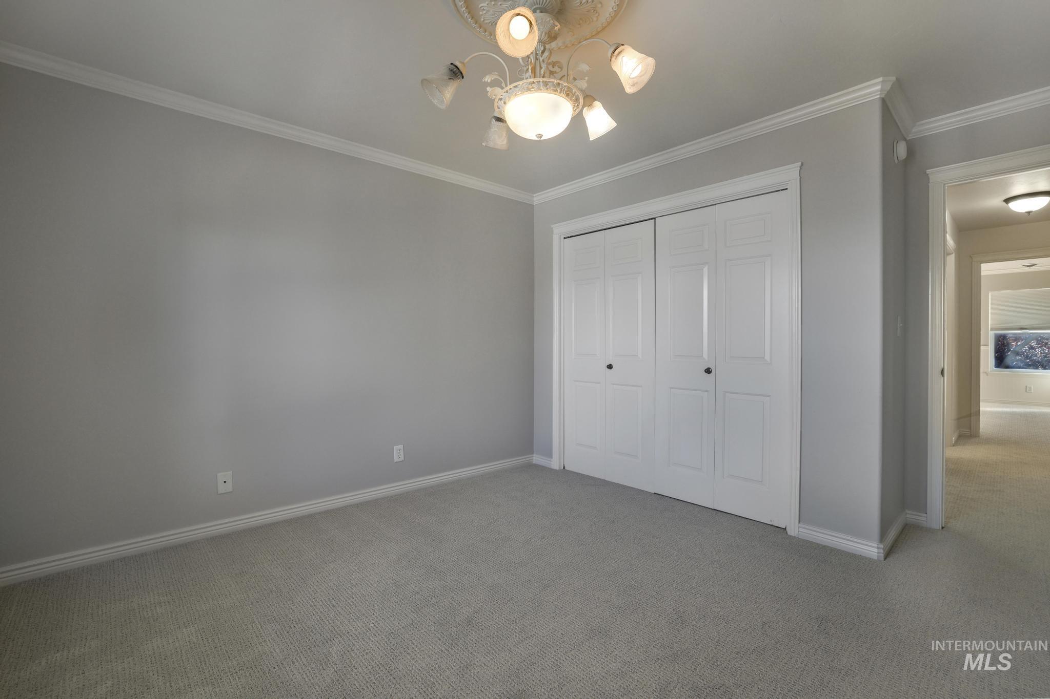 Unfurnished bedroom with ornamental molding, carpet, a closet, and a chandelier