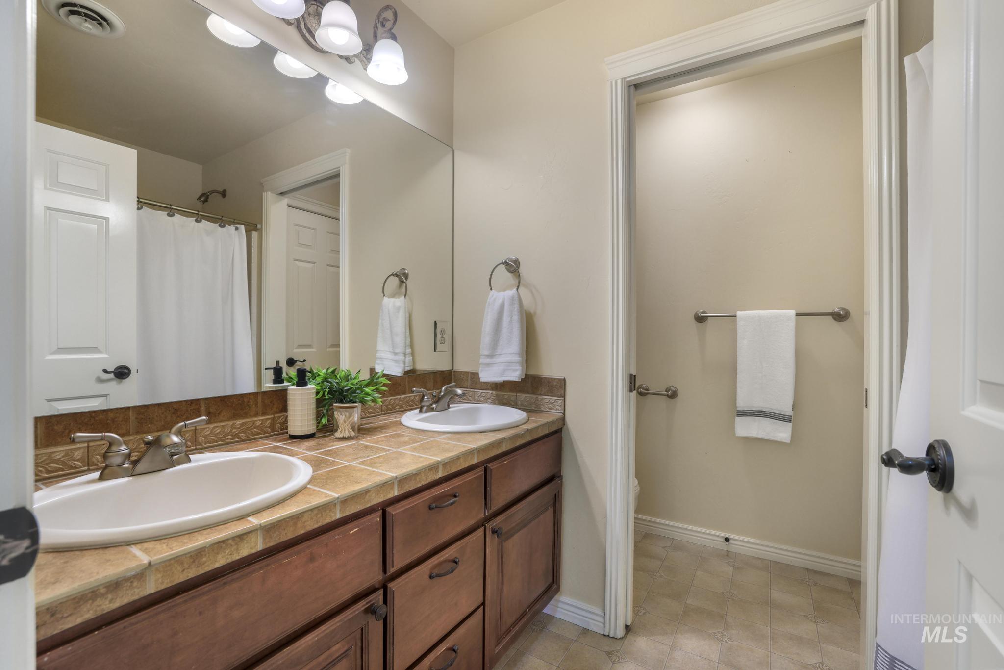 Full bathroom with double vanity, a shower with shower curtain, and light tile patterned flooring