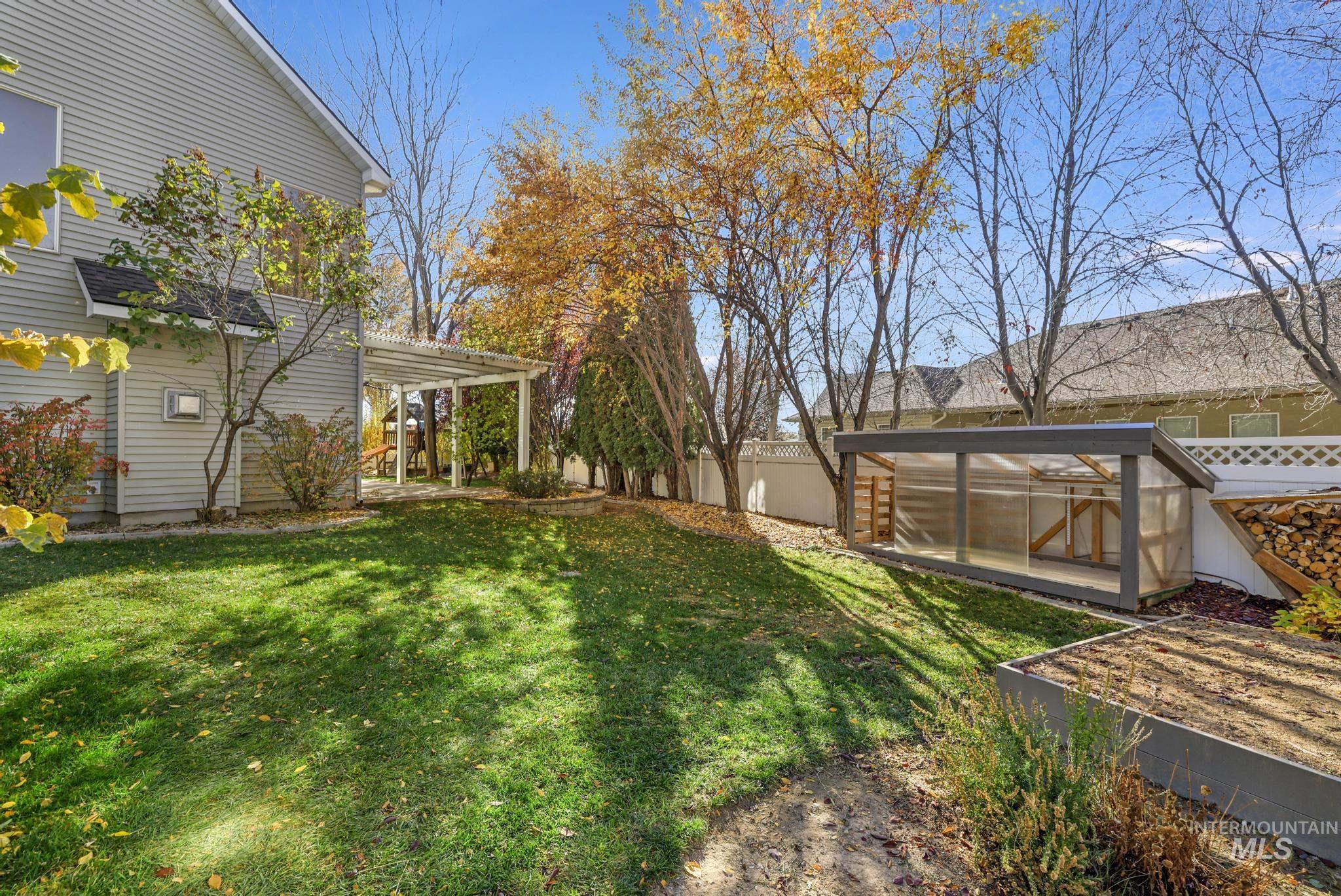 Fenced backyard featuring a greenhouse and an outdoor structure