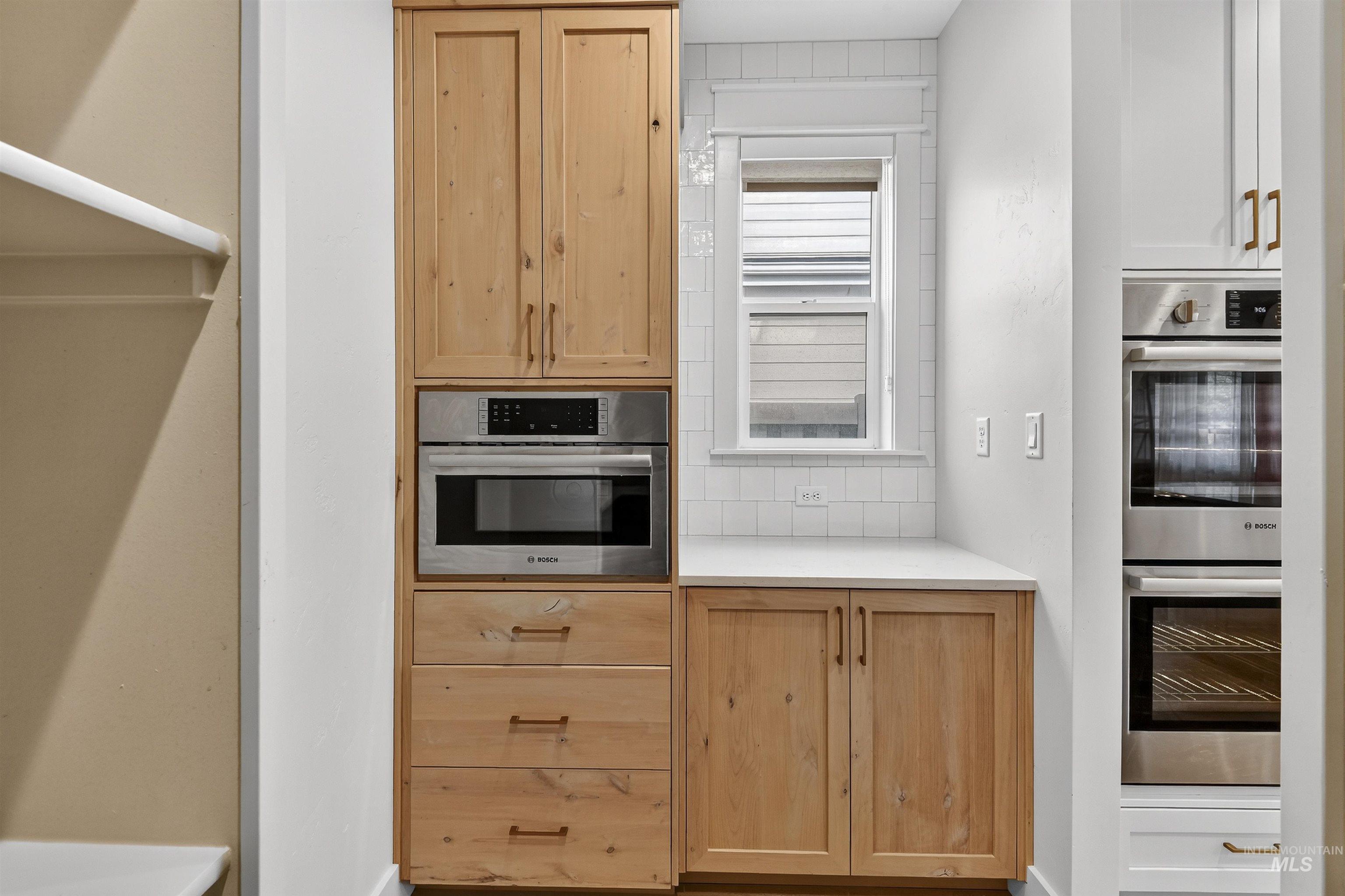 Kitchen with light brown cabinetry, double oven, light countertops, and tasteful backsplash