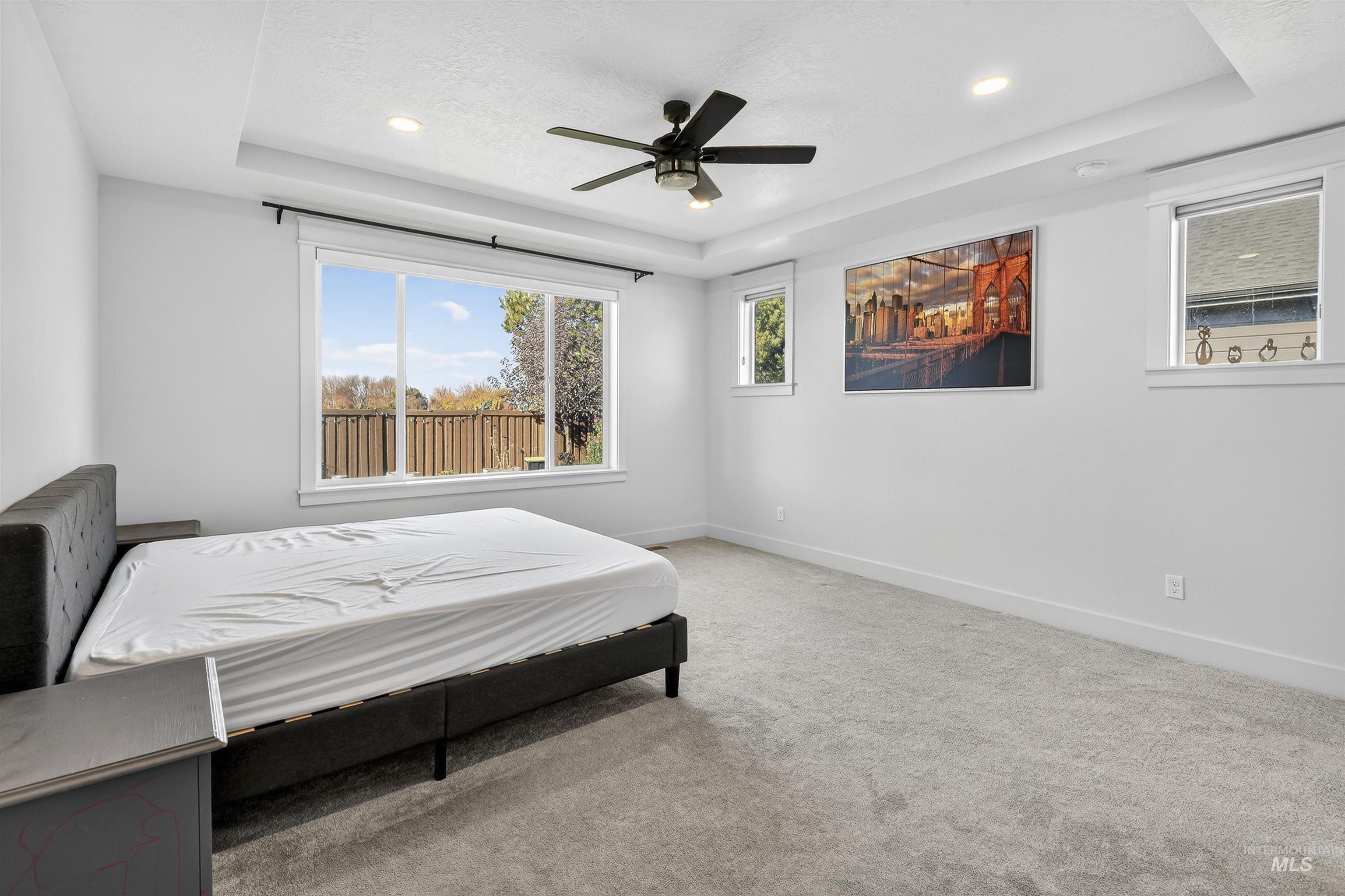 Bedroom featuring a tray ceiling, light carpet, multiple windows, a ceiling fan, and recessed lighting