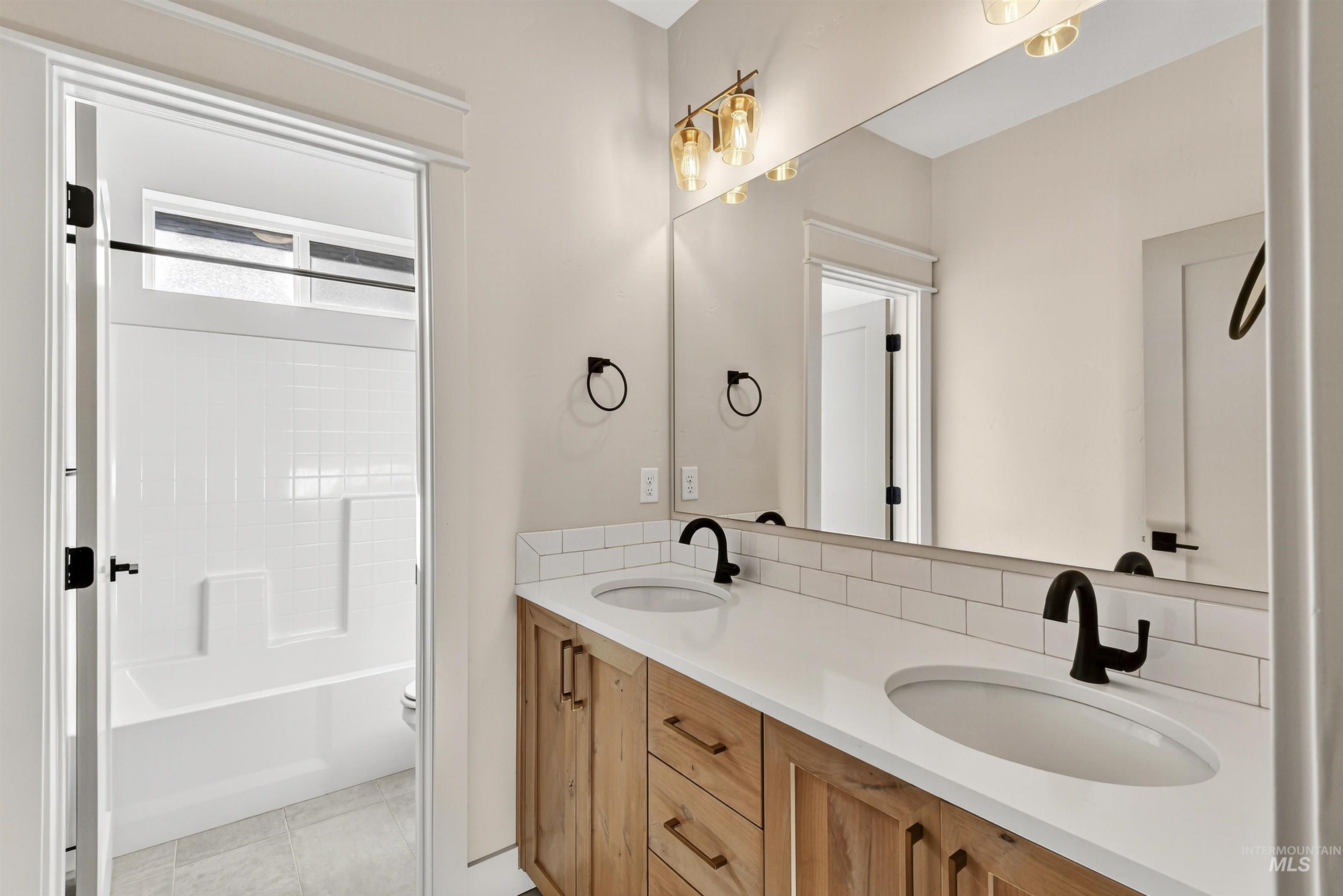 Full bath featuring double vanity, light tile patterned flooring, and shower / washtub combination