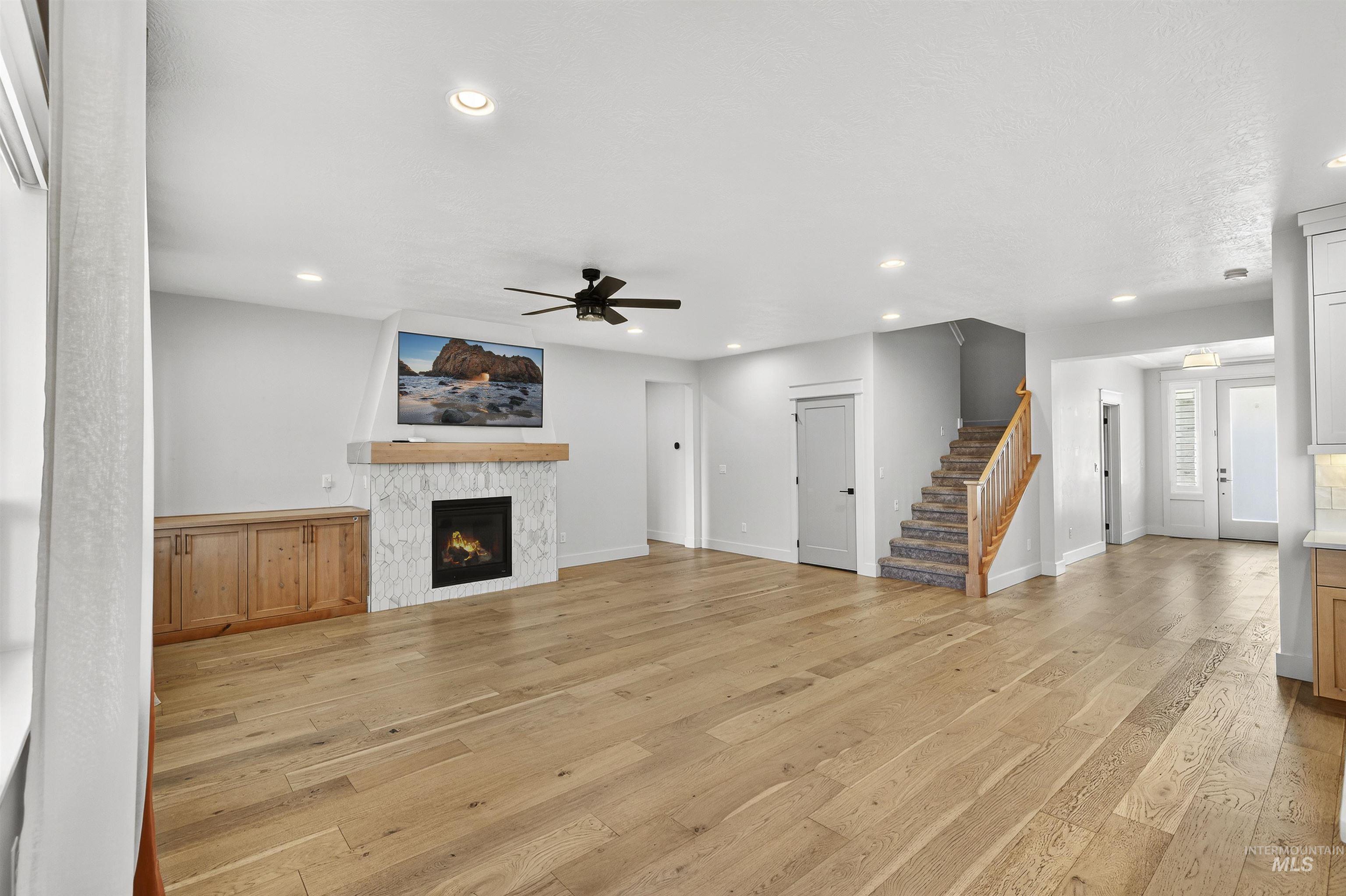 Unfurnished living room featuring stairway, light wood finished floors, a lit fireplace, a ceiling fan, and recessed lighting