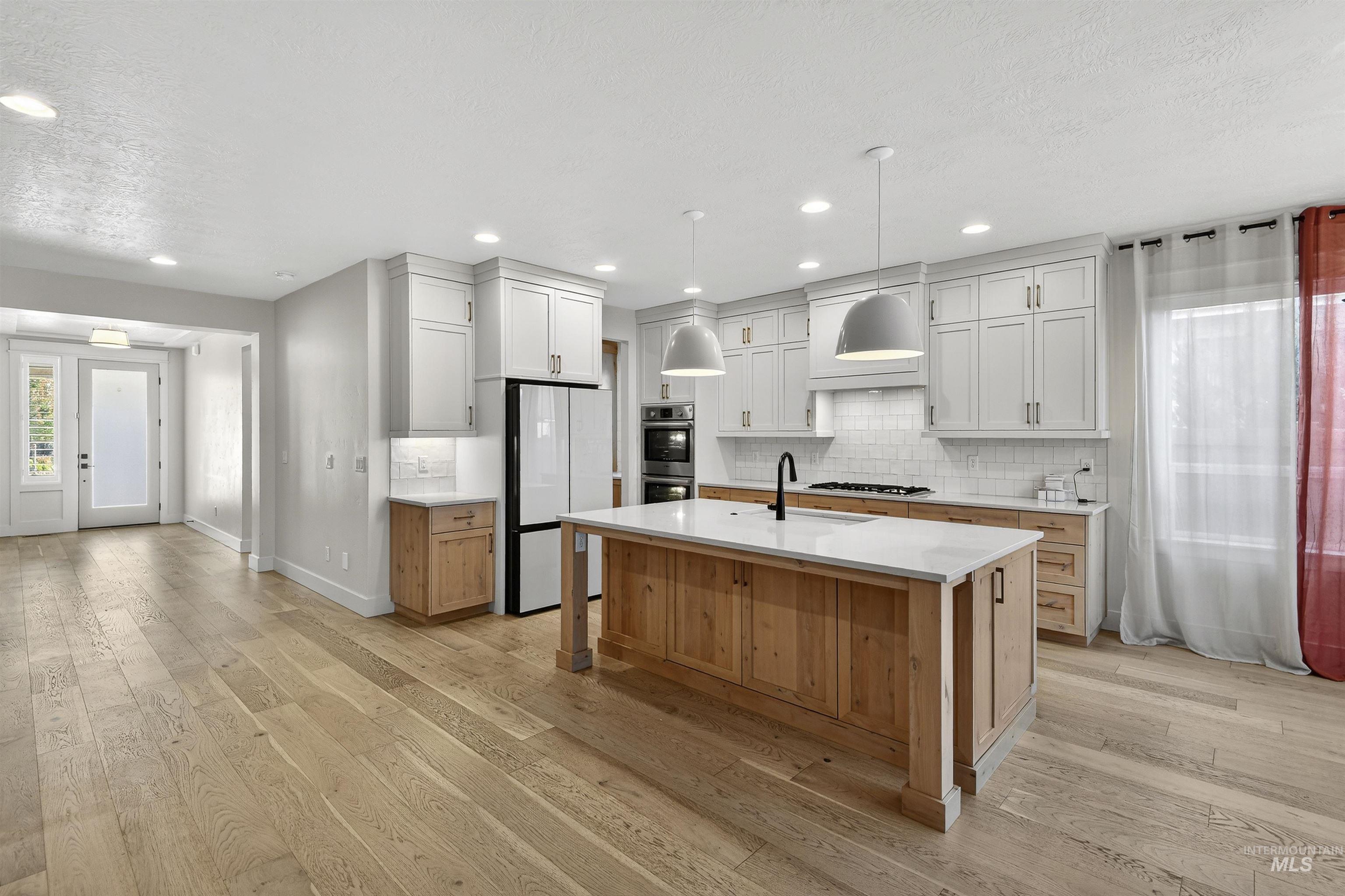 Kitchen featuring freestanding refrigerator, decorative backsplash, an island with sink, light wood-style floors, and decorative light fixtures