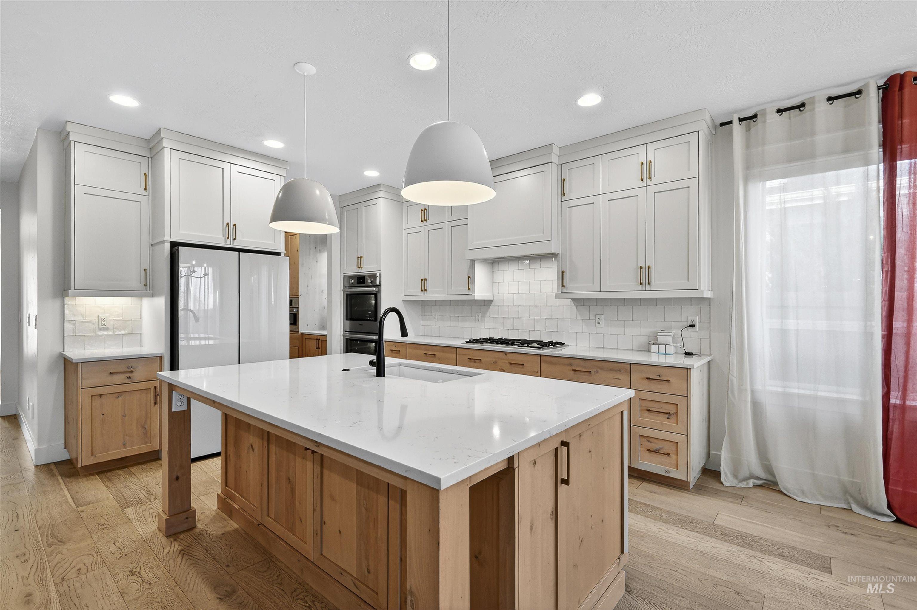 Kitchen featuring hanging light fixtures, light wood-style flooring, light brown cabinetry, white appliances, and light stone countertops