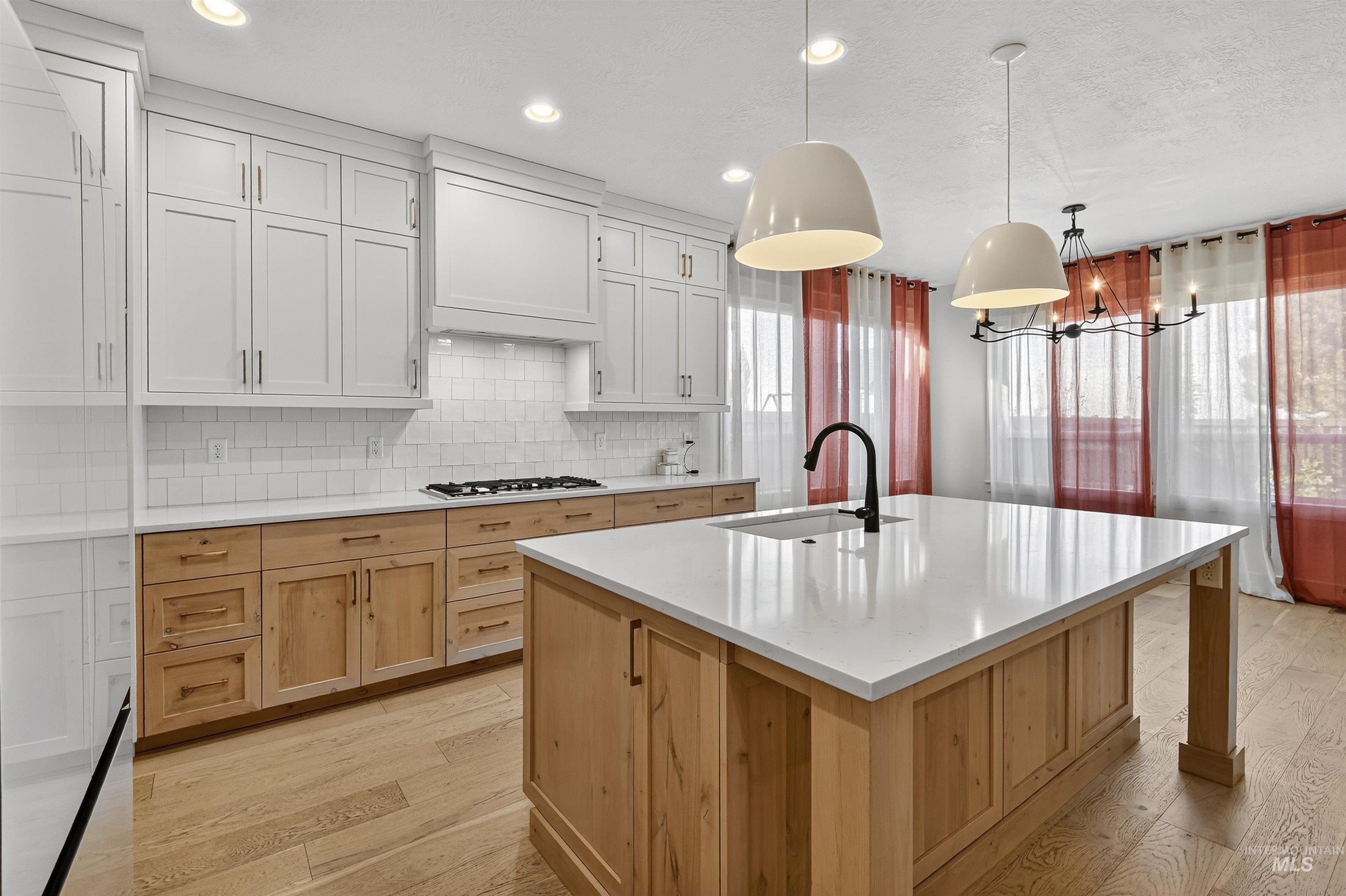 Kitchen featuring light wood-style flooring, built in fridge, decorative light fixtures, light brown cabinets, and backsplash