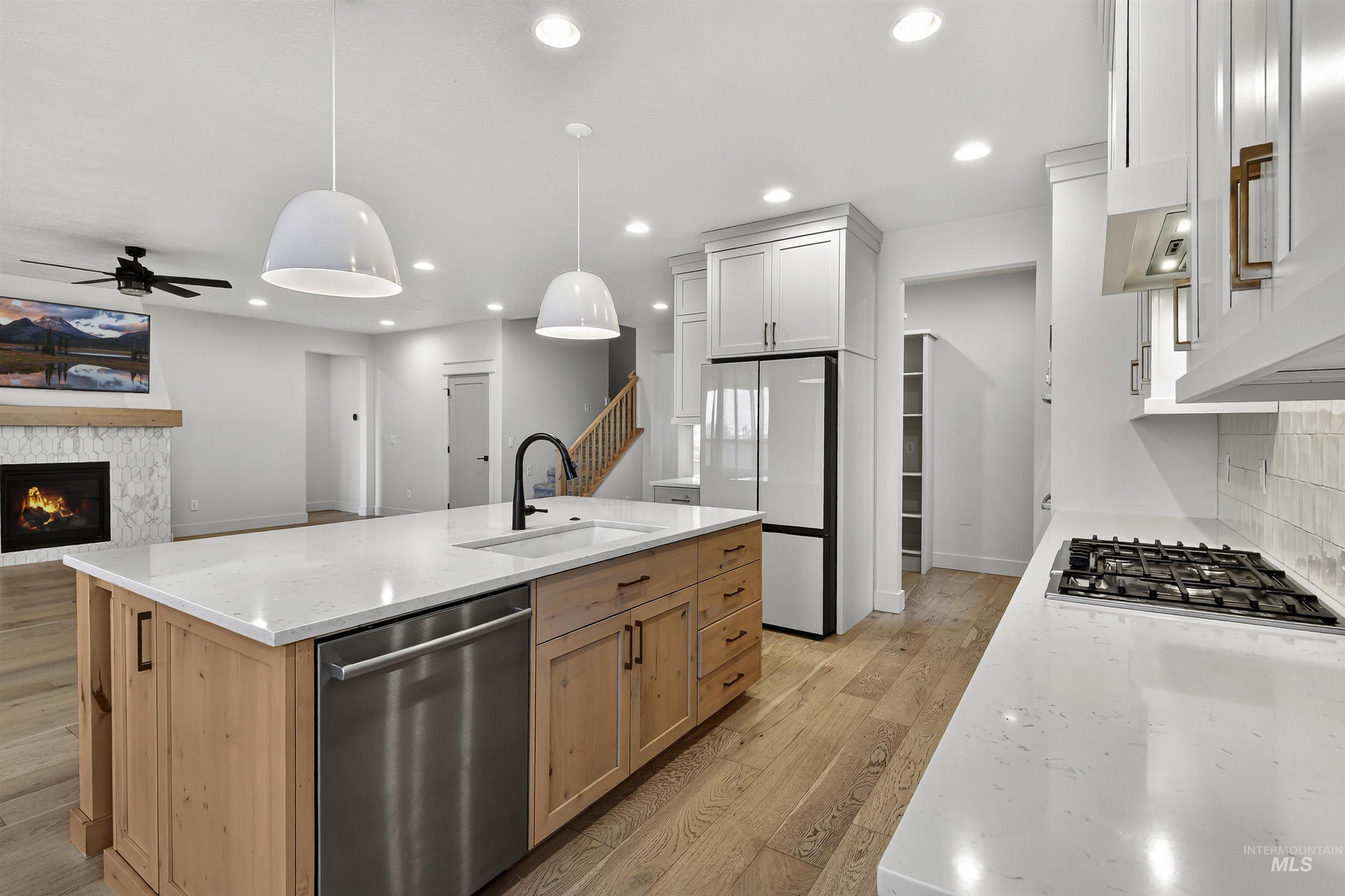 Kitchen with light wood-type flooring, stainless steel appliances, light stone counters, hanging light fixtures, and a ceiling fan